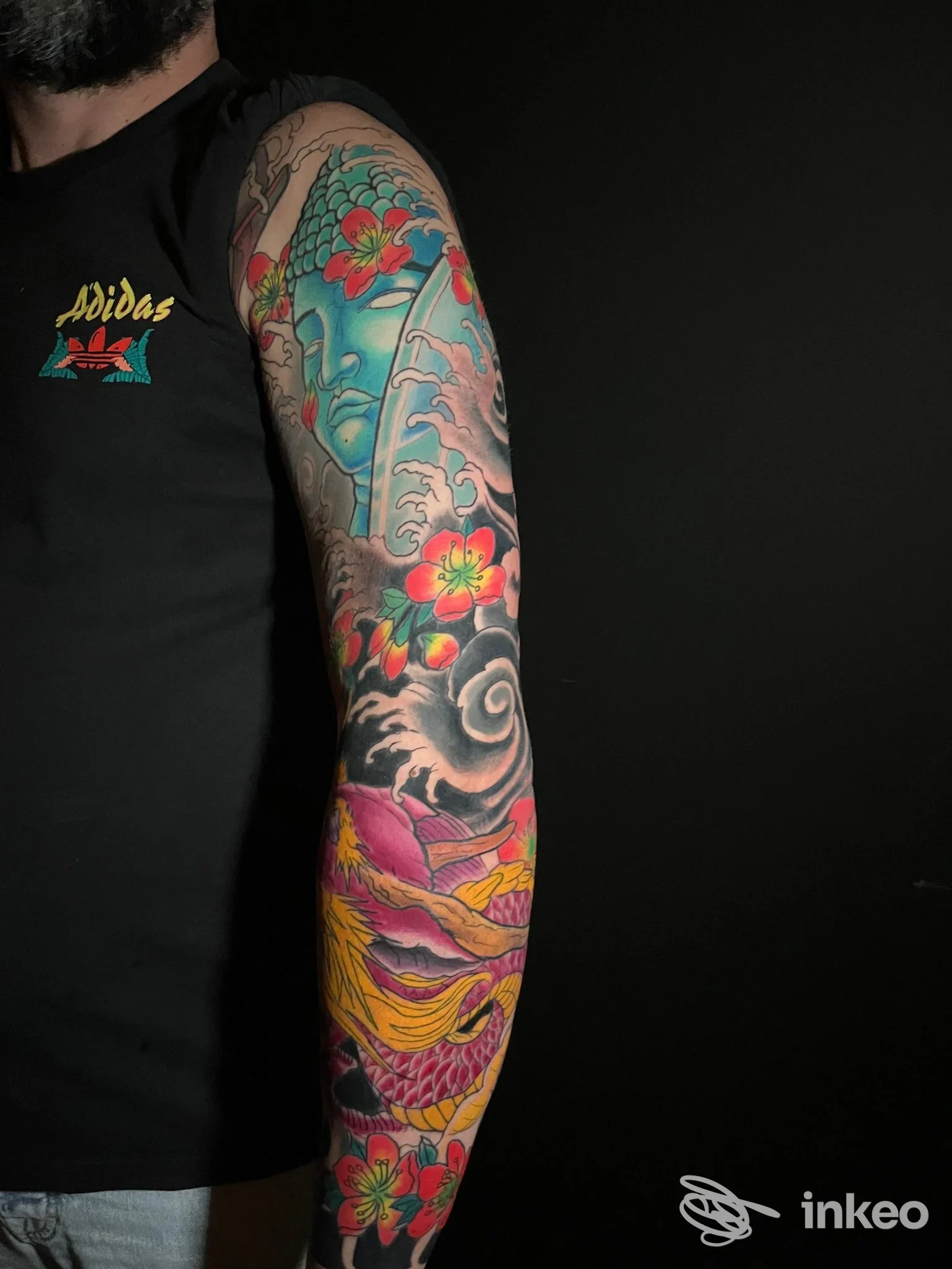 Braccio destro completamente tatuato con motivi colorati, fiori e paesaggi, su sfondo nero; tatuaggio vivace e dettagliato visibile dall’omero fino all’avambraccio, senza volto inquadrato. Studio Amon Ra Tattoo, Calvizzano.