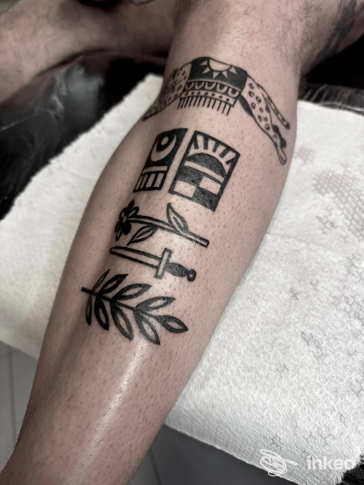 Braccio di una persona con un tattoo visibile in nero che comprende motivi decorativi, spade e foglie, su pelle chiara.