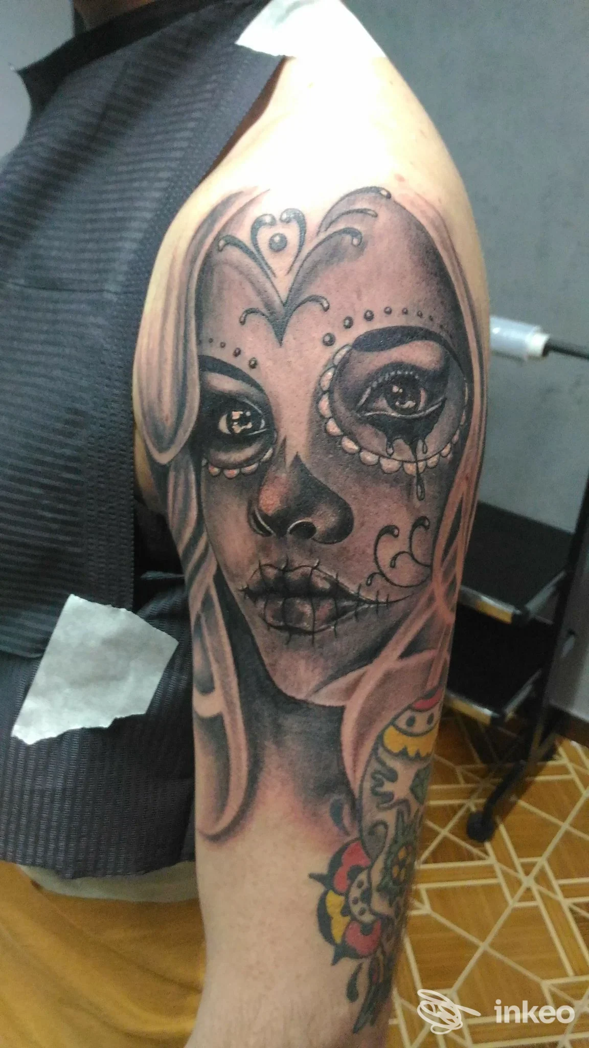Tattoo realistico su avambraccio raffigurante un volto femminile con motivi decorativi tradizionali, realizzato in tonalità grigie e nere.