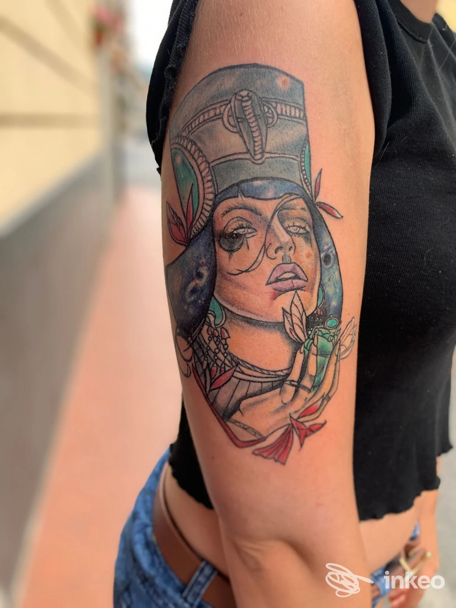 Braccio di una persona con tatuaggio colorato e dettagliato: figura femminile con elmo ornamentale, decorazioni floreali, tratto inchiostrato su pelle, sfondo neutro.