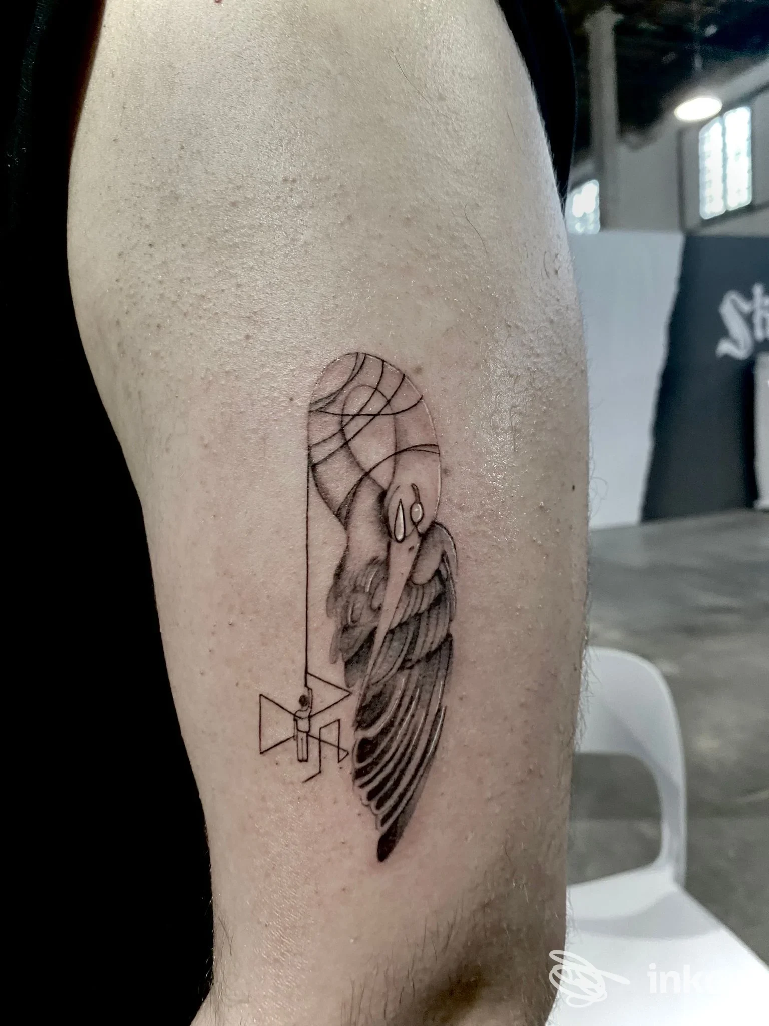 Tatuaggio geometrico in bianco e nero su avambraccio: linea di contorni nette, piuma stilizzata con motivi geometrici, eseguito su pelle. Presente cornice di un retro della stanza.