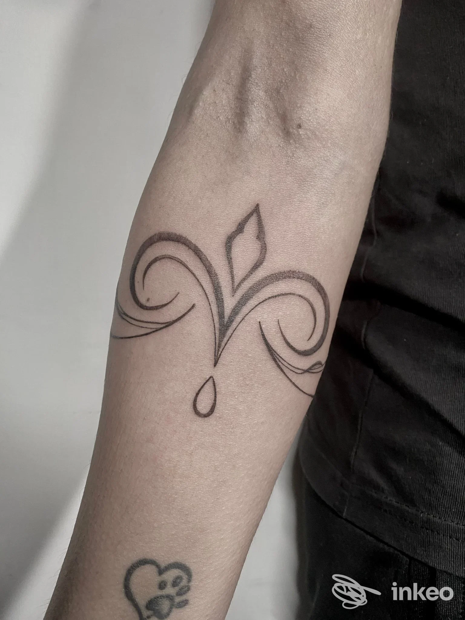 Avambraccio visibile con tatuaggio lineare di stile floreale, linee nere sottili e una goccia; si vede parte della maglietta e della pelle, studio InkFerno Tattoo, Nocera Inferiore.