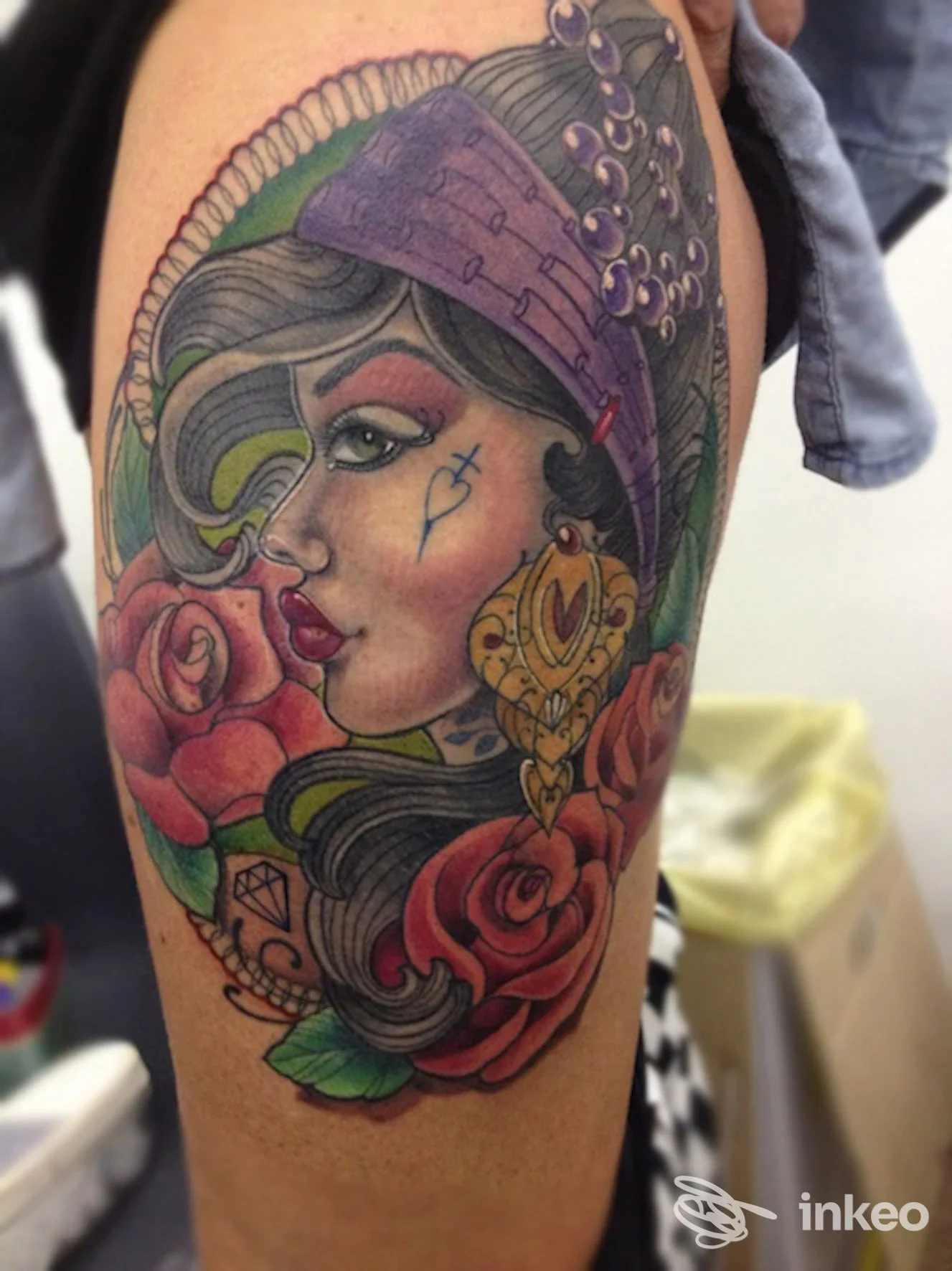 Tattoo visibile su braccio raffigurante una donna con cappello viola e fiori rossi, colori vivaci e linee nette su pelle reale.