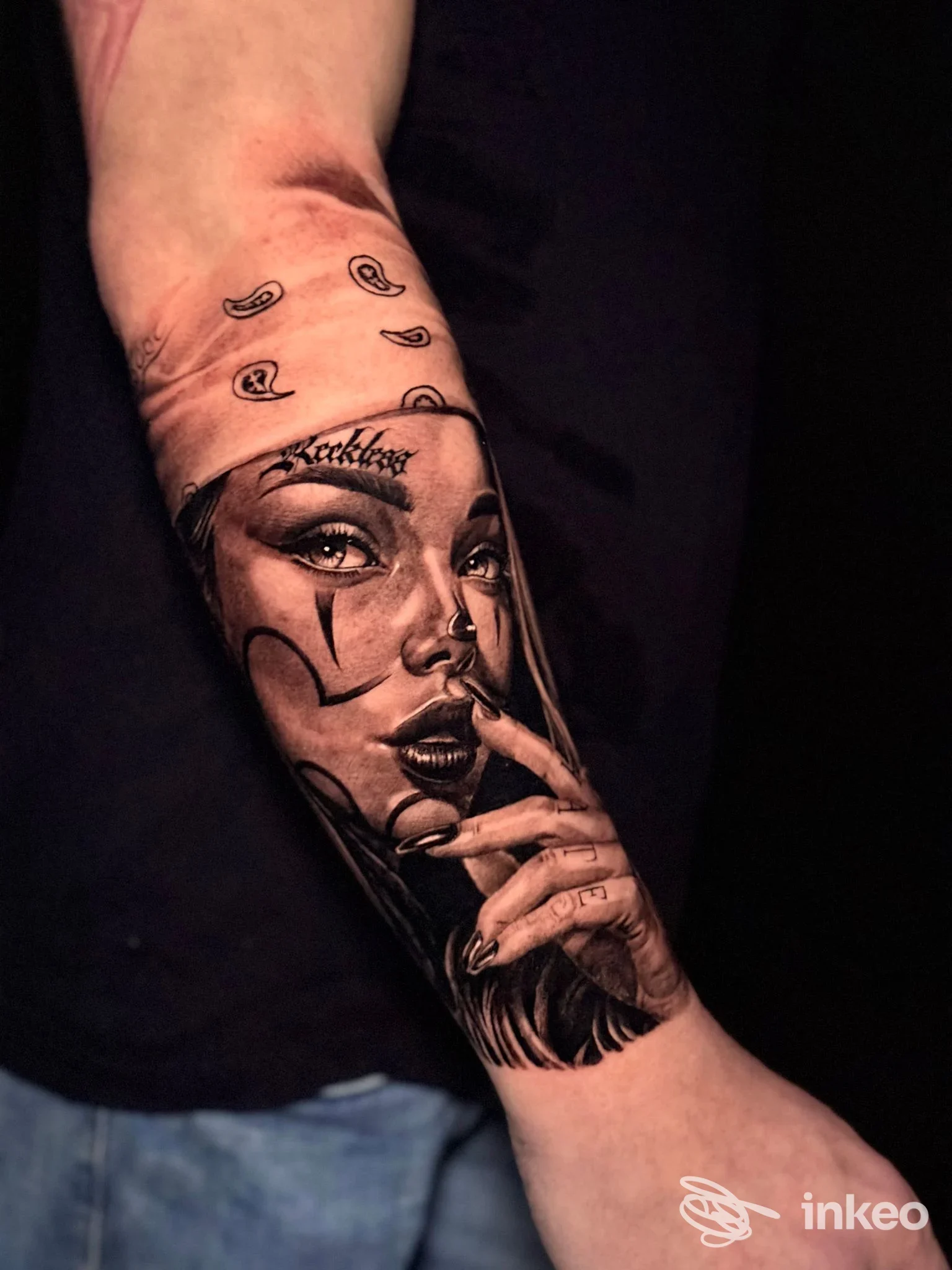 Avambraccio raffigurante un ritratto femminile in bianco e nero, eseguito come tatuaggio realistico con contorni marcati e dettagli definito sul volto e sulle mani.