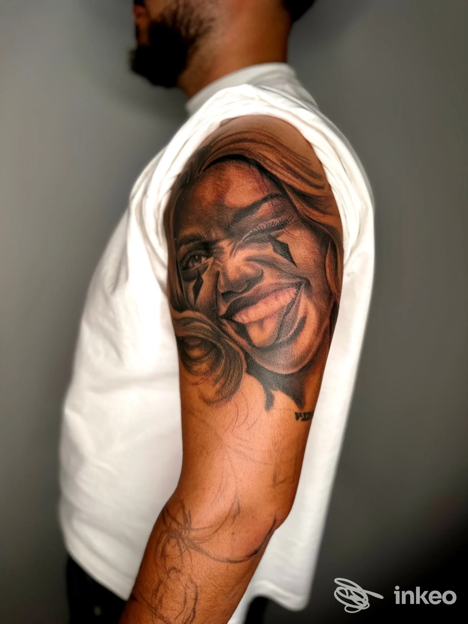 Braccio di un uomo con tatuaggio ritagliato sul braccio, dettaglio di ritratti e linee scure su pelle chiara, visto di profilo.