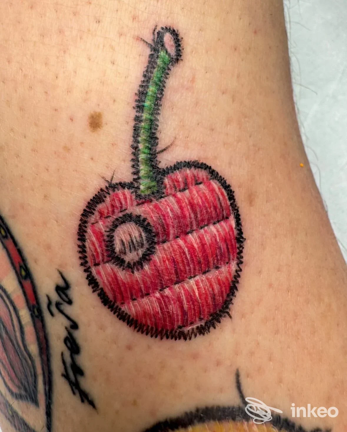 Tatuaggio visibile su pelle raffigurante una ciliegia rossa con contorni neri, realizzato in stile cartoonesco/old school sull’avambraccio, colorato con sfumature rosse e verde sulla crosta del gambo.