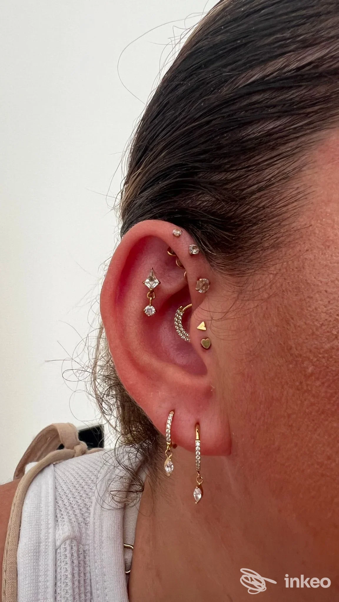 orecchio sinistro con più piercing dorati tra cui anello a cerchio, ciondino a goccia e piccole puntiformi, visibili sul lobo e su tessitura del padiglione, foto ravvicinata di prova studio Dairolotopiercing a Frattamaggiore