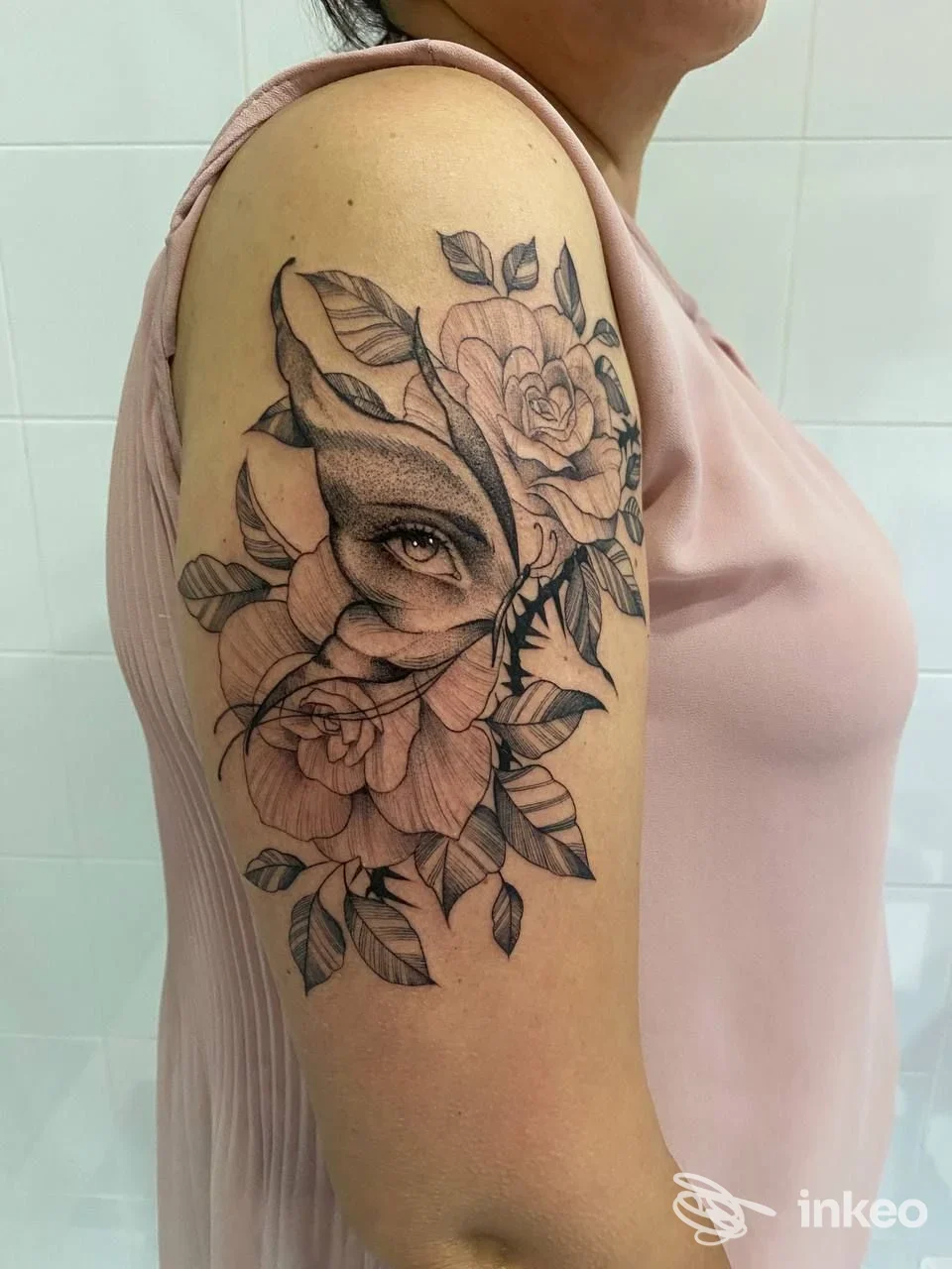 Tattoo realistico sul braccio raffigurante fiori e una figura animale stilizzata, linea pulita e sfumature in bianco e nero, visibile su una persona che indossa una maglietta rosa.