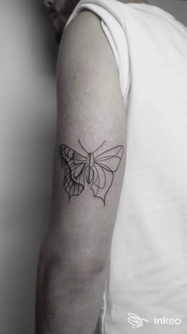 Tattoo sul braccio di una persona: disegno stilizzato di una farfalla con linee nette su pelle nuda.