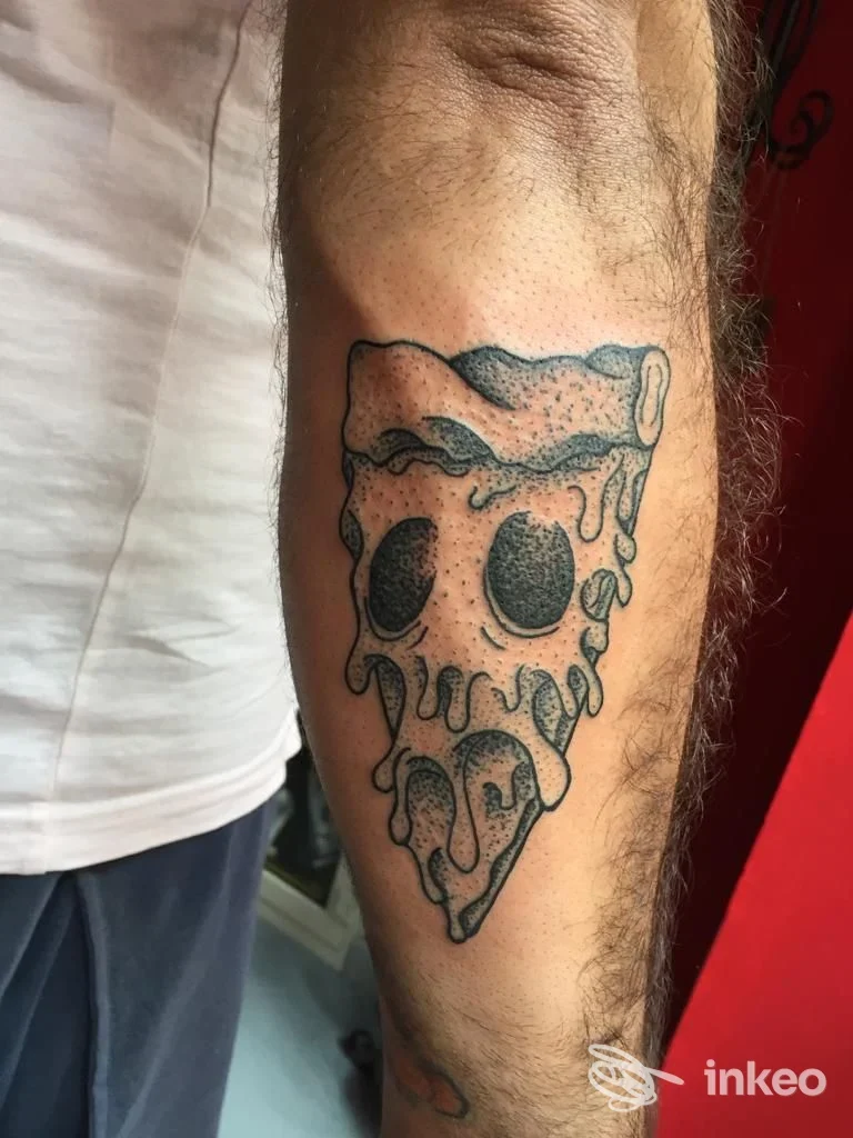 Braccio con tattoo raffigurante una fetta di pizza stilizzata, con marmellature e schizzi di formaggio che cadono, eseguito sulla pelle; tatuaggio in stile linework e shading in bianco/nero sul braccio.