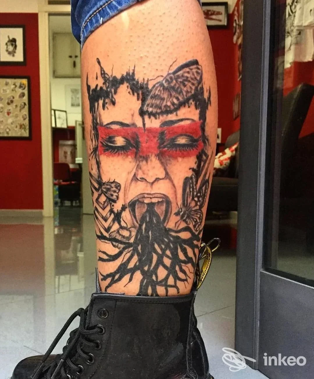 Tattoo sul polpaccio raffigurante un volto umano con elementi decorativi e linee nere, realizzato in stile realistico su pelle.