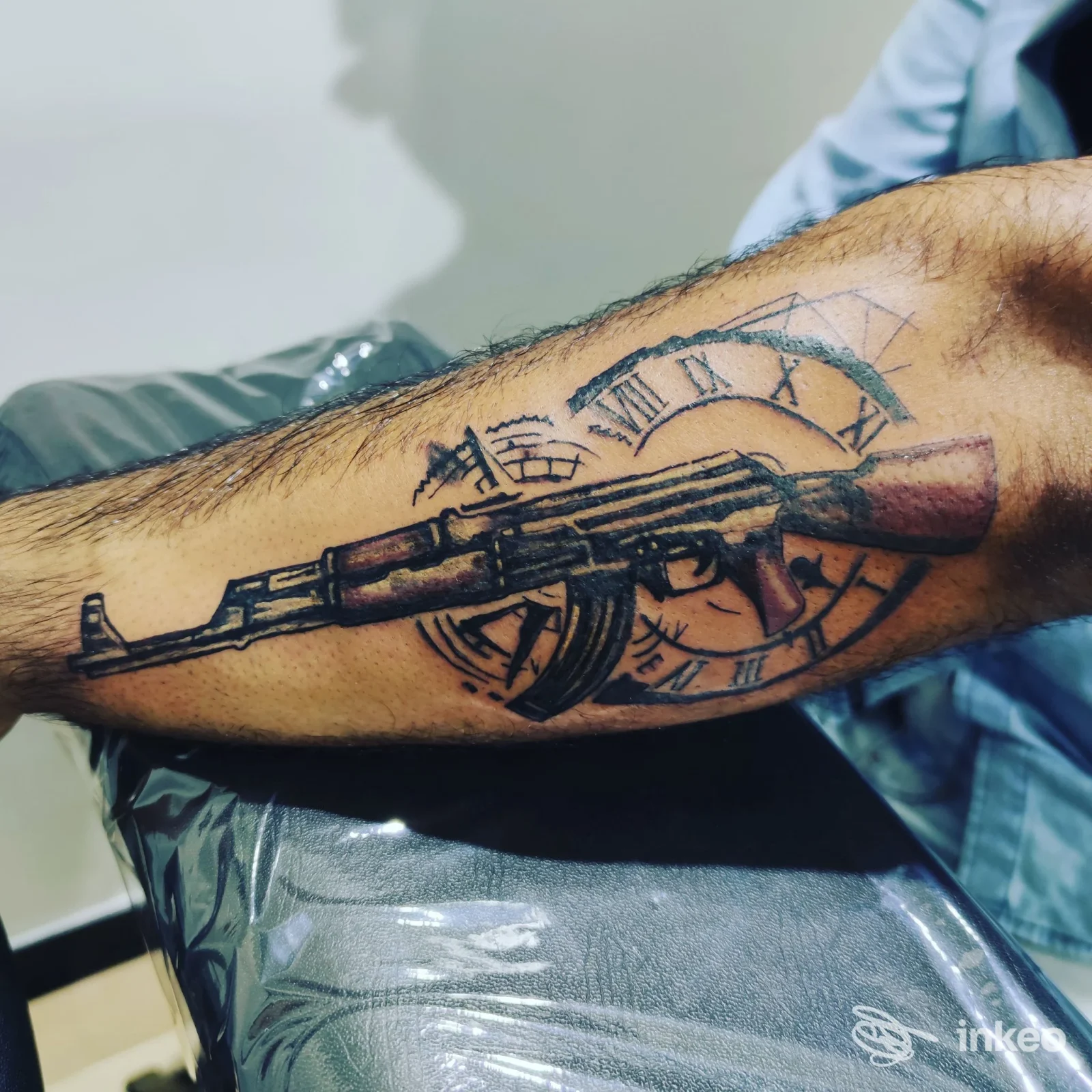 Tattoo sul braccio raffigurante un fucile e un orologio circolare, realizzato presso Serafina’s Ink a Eboli.