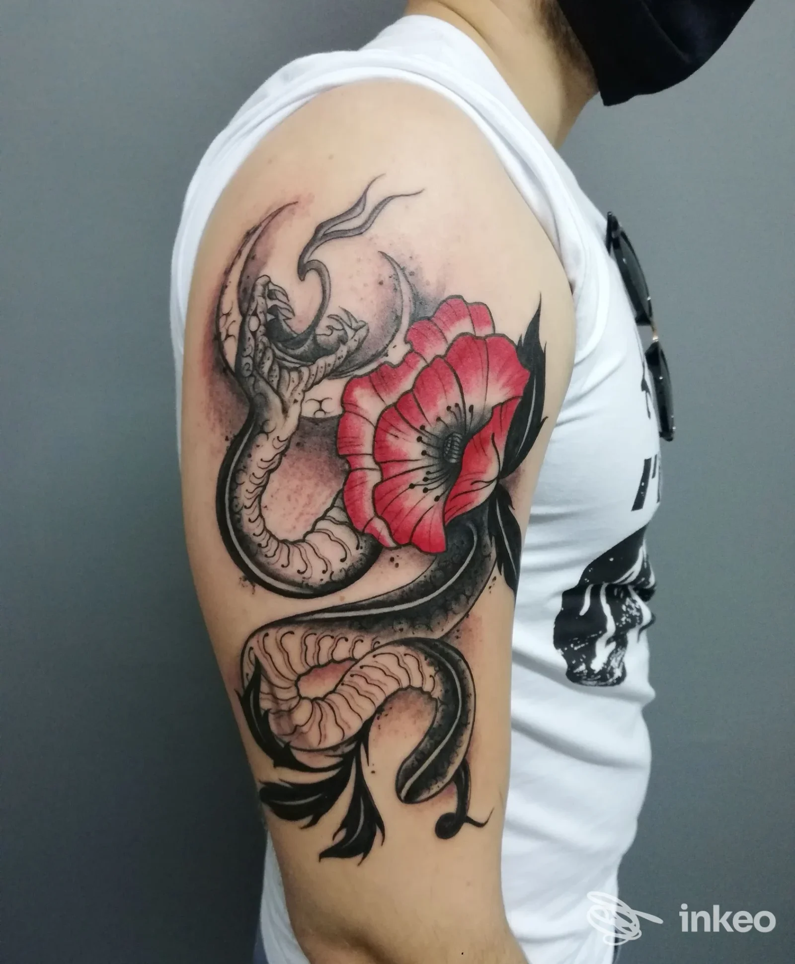 Tatuaggio visibile sul braccio: serpente stilizzato insieme a un grande papavero rosso, realizzato sulla pelle di una persona. Studio Officine D'agostino Tattoo a Mercato San Severino.