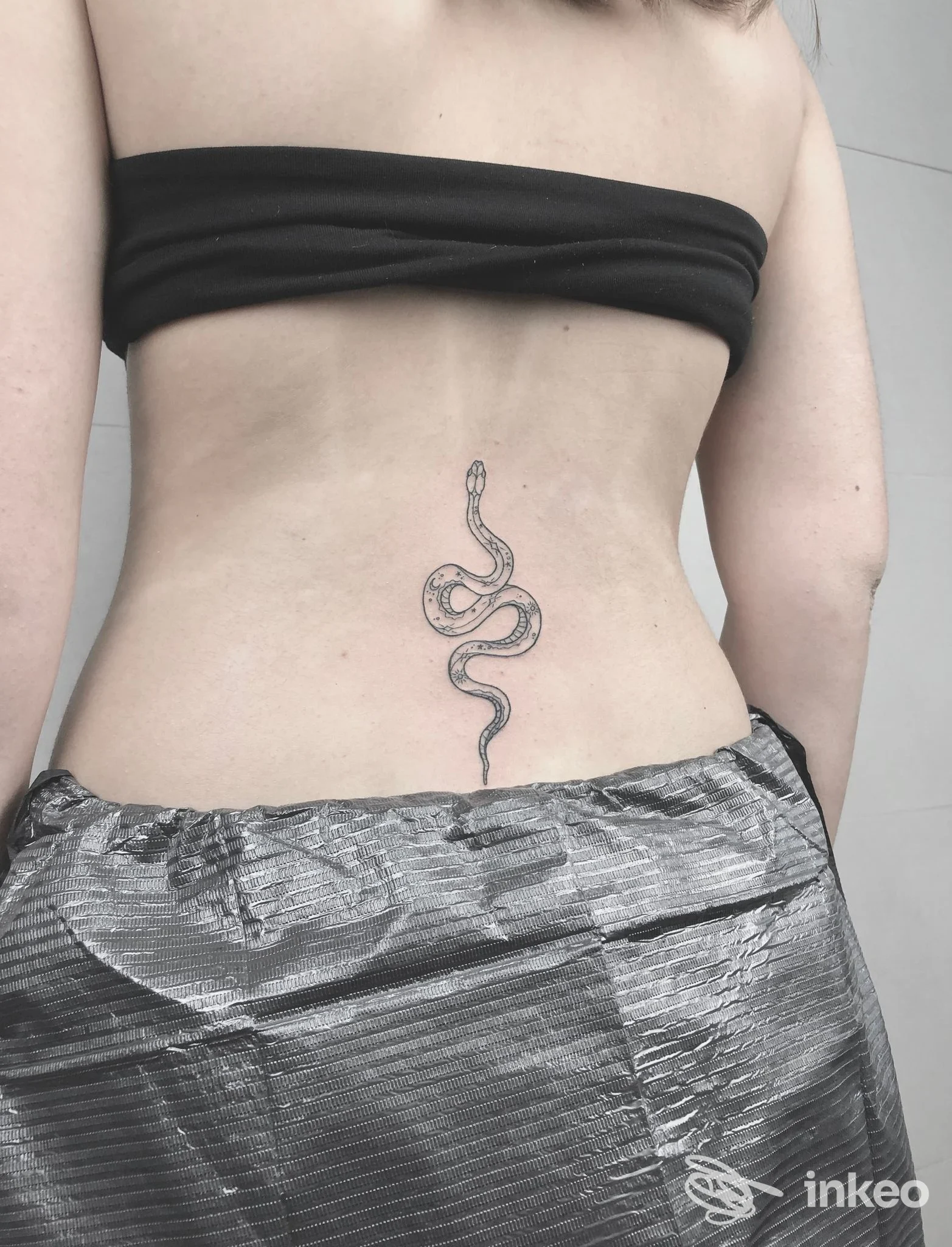 Schiena di una persona con un tatuaggio a serpente lungo la colonna vertebrale, visibile dalla vita al dorso, nello studio Play Tattoo a Napoli.