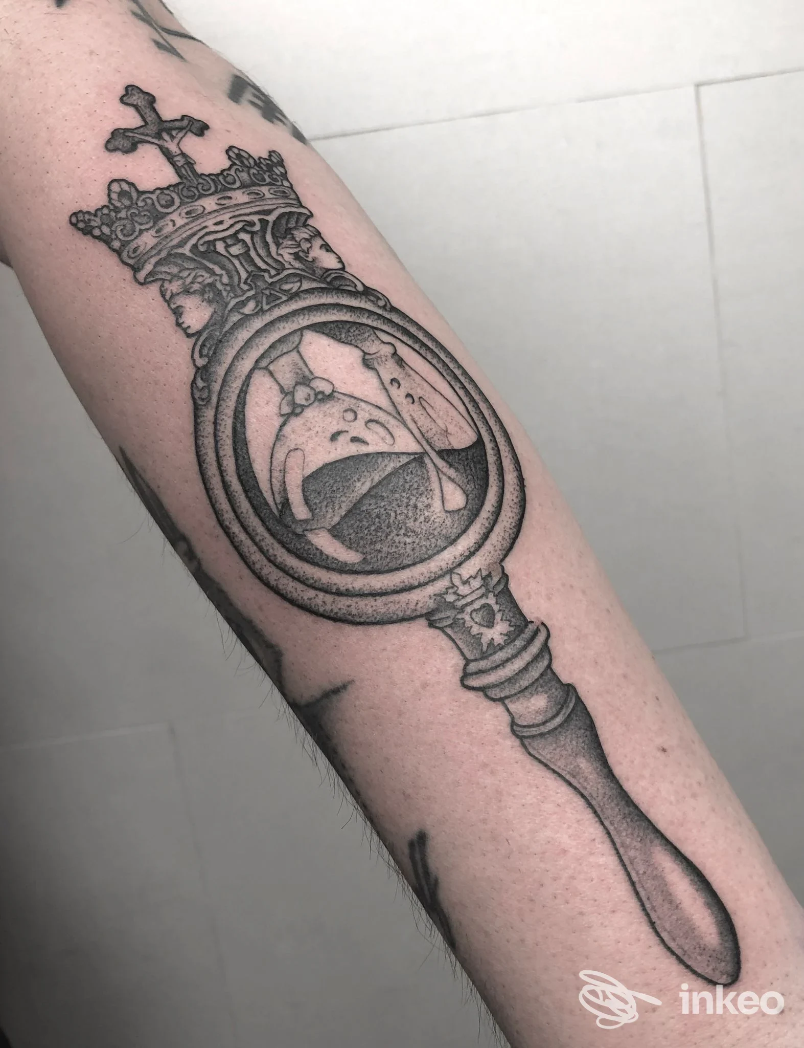 Tatuaggio sul braccio raffigurante una clessidra incastonata in un medaglione ornato con fodero a forma di pugnale, eseguito in stile linework su pelle chiara.