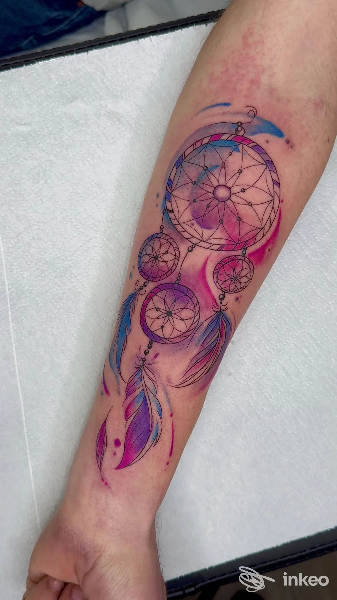 Avambraccio con tatuaggio colorato a tema dreamcatcher: cerchi intrecciati, pennacchi blu e rosa, sfondo sfumato, firma studio GEME Art Ottaviano non visibile.