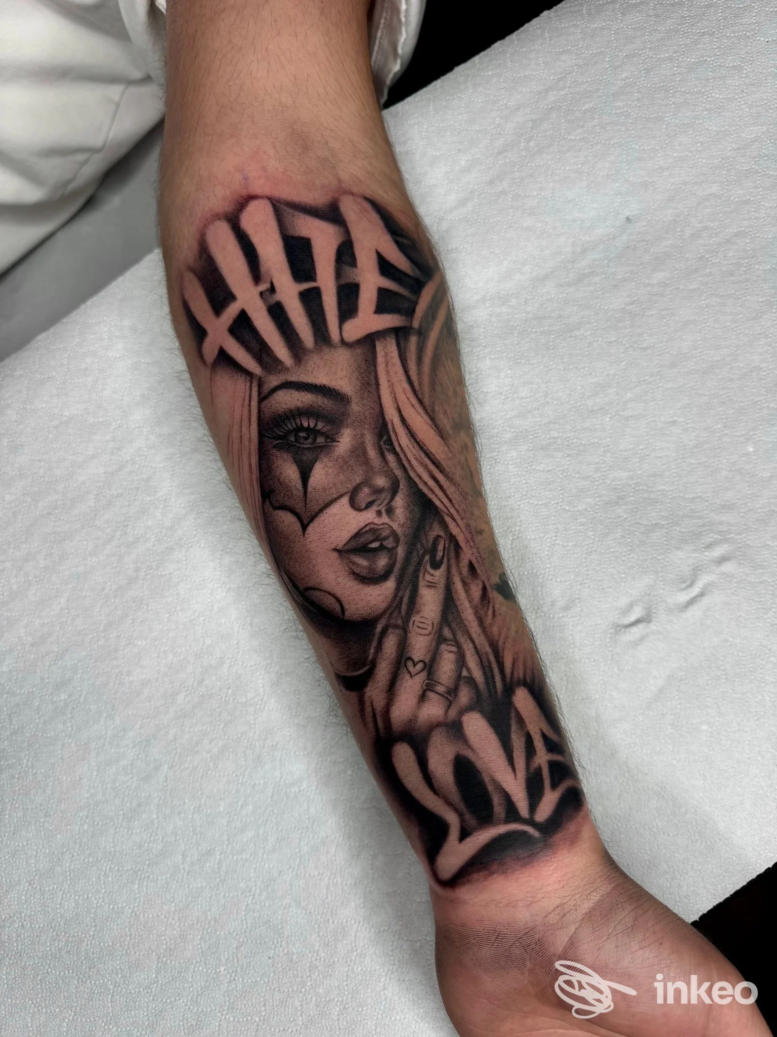 Tatuaggio realistico sull’avambraccio raffigurante un volto femminile con cappuccio, tonalità scure e dettagli anatomici