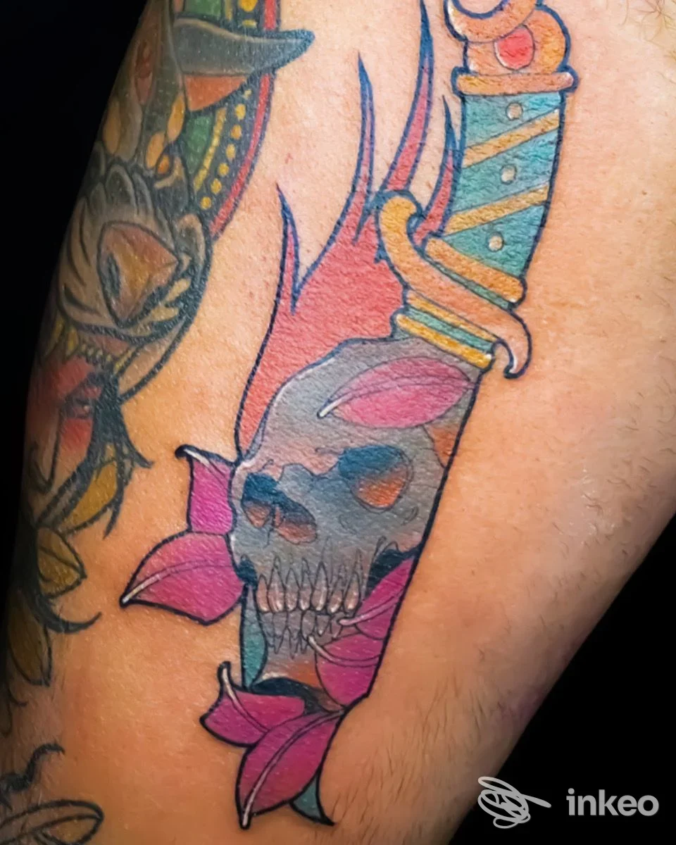 Tattoo colorato su avambraccio raffigurante una figura scheletrica con coltello, contorni neri e sfumature blu-rosa, visibile su pelle in studio Risk Tattoo Studio a Frattamaggiore.
