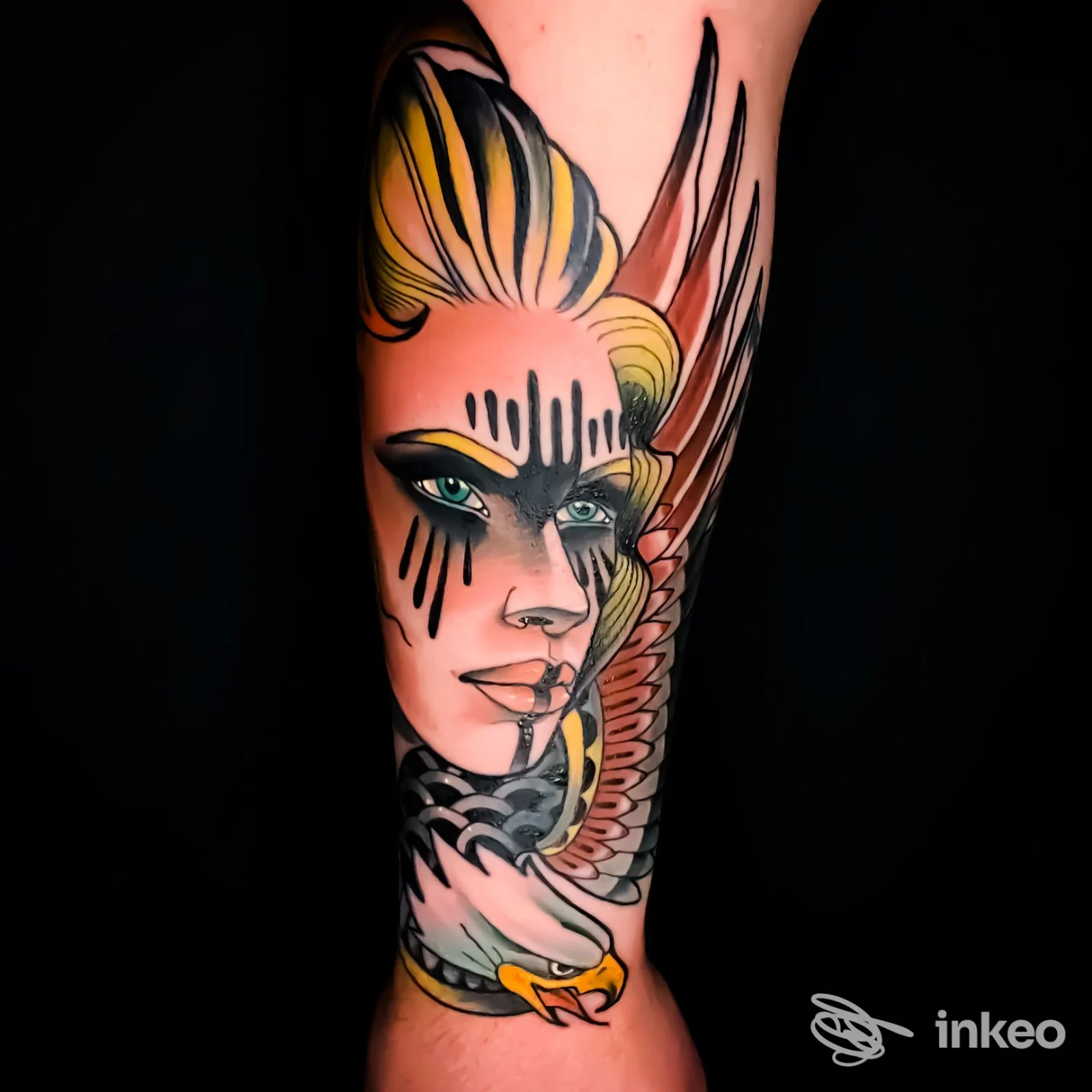 Tattoo sul braccio raffigurante una testa femminile stilizzata con ali colorate, linee marcate e colori vividi su sfondo scuro.