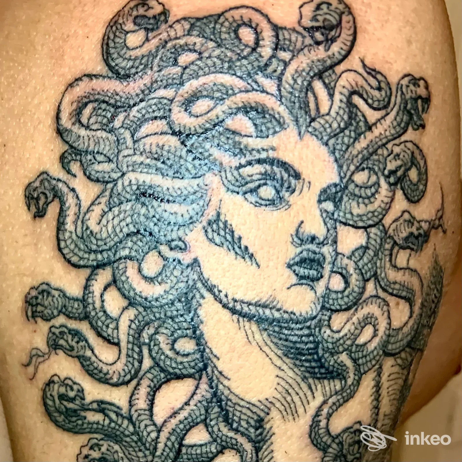 Tattoo sul braccio raffigurante una testa femminile con serpenti intrecciati tra i capelli, dettaglio in nero/blu su pelle.
