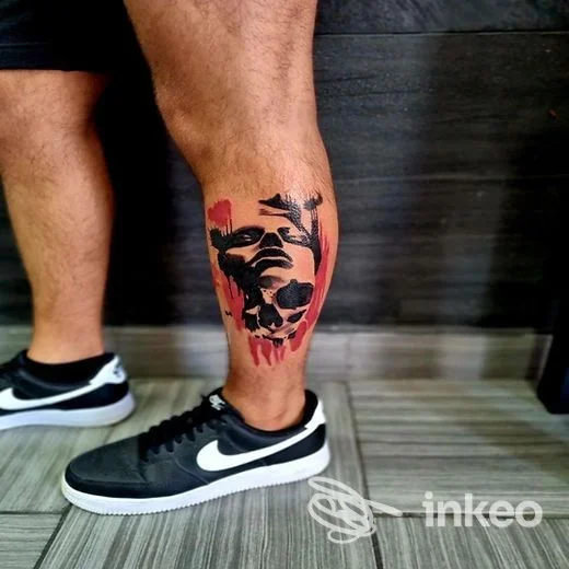 Tatuaggio visibile sulla gamba di una persona, con sfondo pavimentato; stile grafico in bianco e rosso, parte del polpaccio è tatuata.