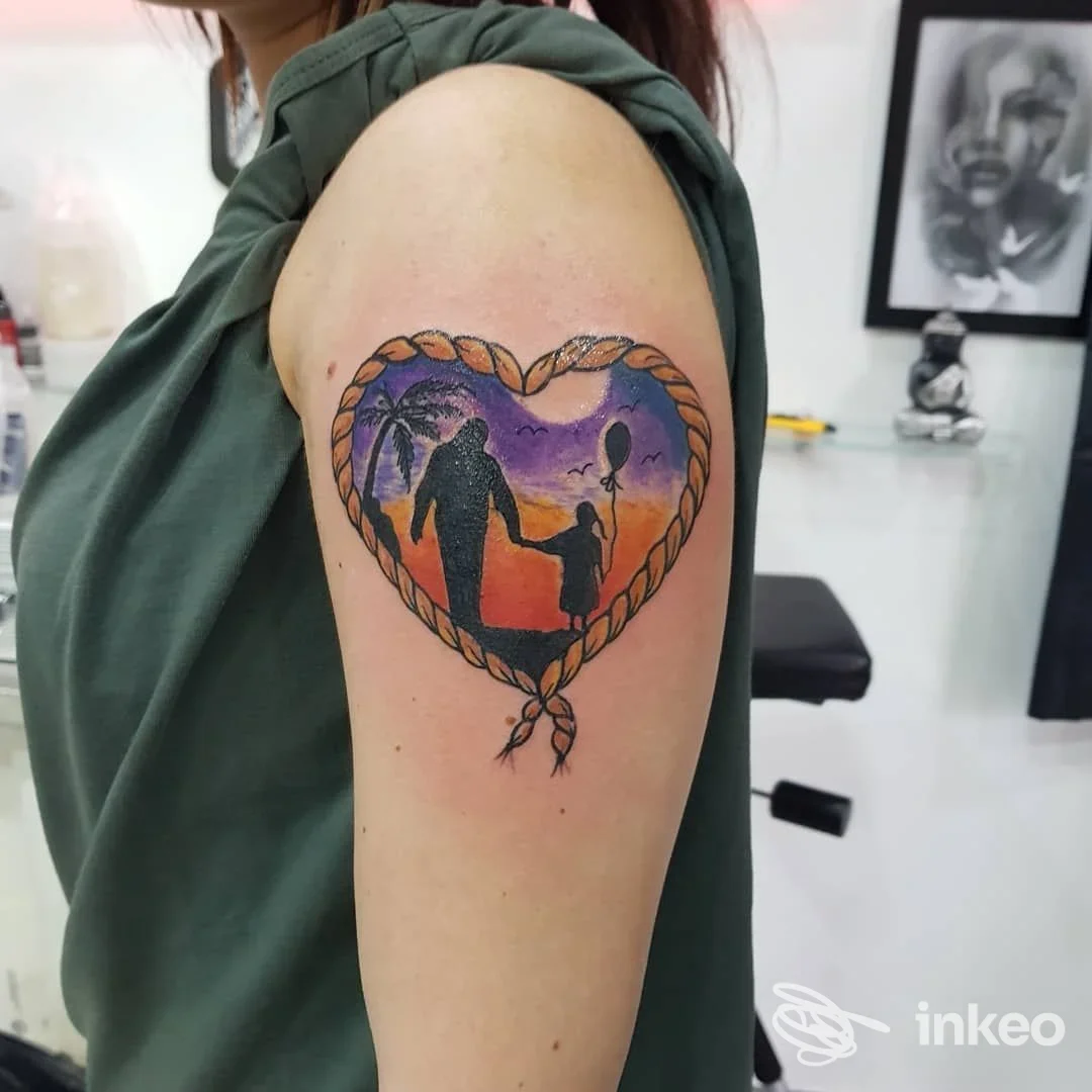 Tatuaggio colorato su braccio raffigurante un cuore intrecciato con corde, contenente silhouette di persone a coppia al tramonto; realizzato sulla pelle presso La Fenice Tattoo Ink, Napoli.