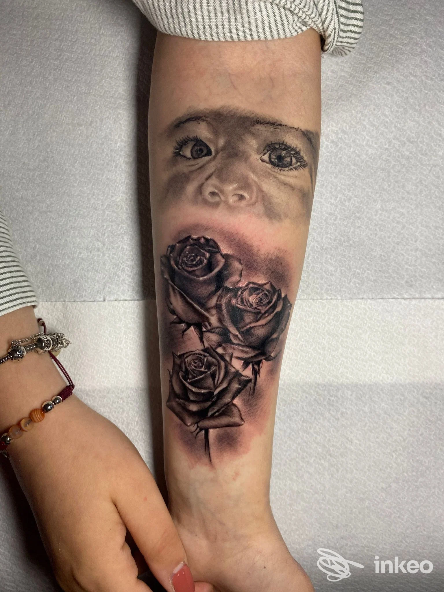 Tatuaggio realistico sull'avambraccio raffigurante rose e un volto integrato nel disegno, realizzato presso Ziomesti Tattoo Studio a Scafati.