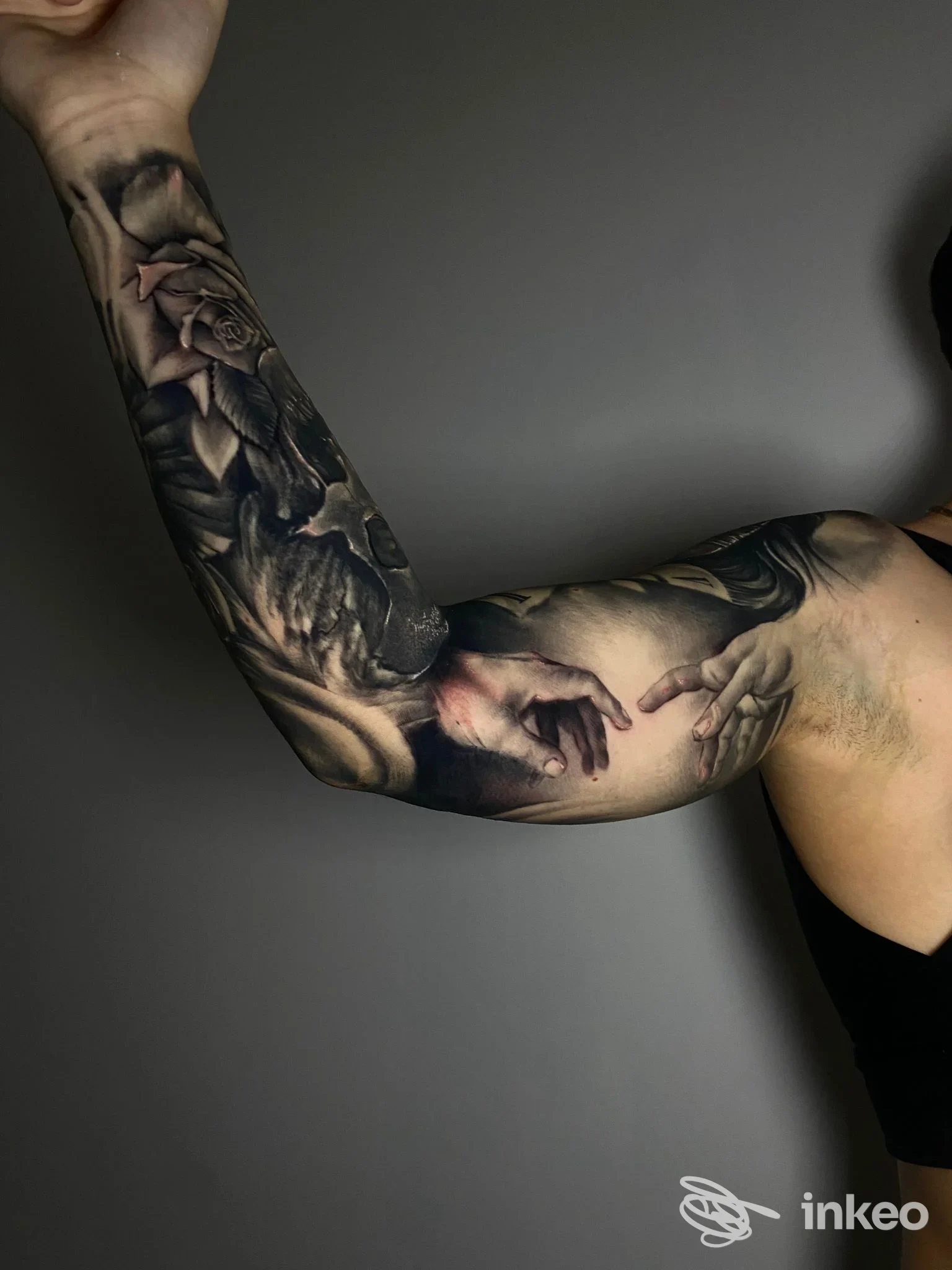 Braccio coperto da tatuaggio realistico con mani e rosa, tonalità scure su sfondo grigio. Ritratto di lavoro di Ziomesti Tattoo Studio a Scafati.