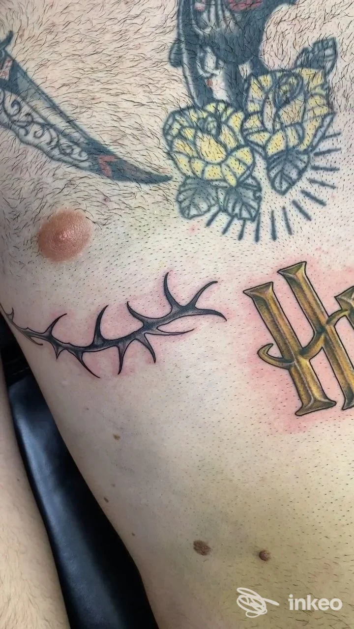 Davidoff Tattoo Studio, Cava de' Tirreni: veduta ravvicinata di tatuaggio su pelle con fiori gialli e neri, lama affilata e lettere dorate sull'avambraccio.