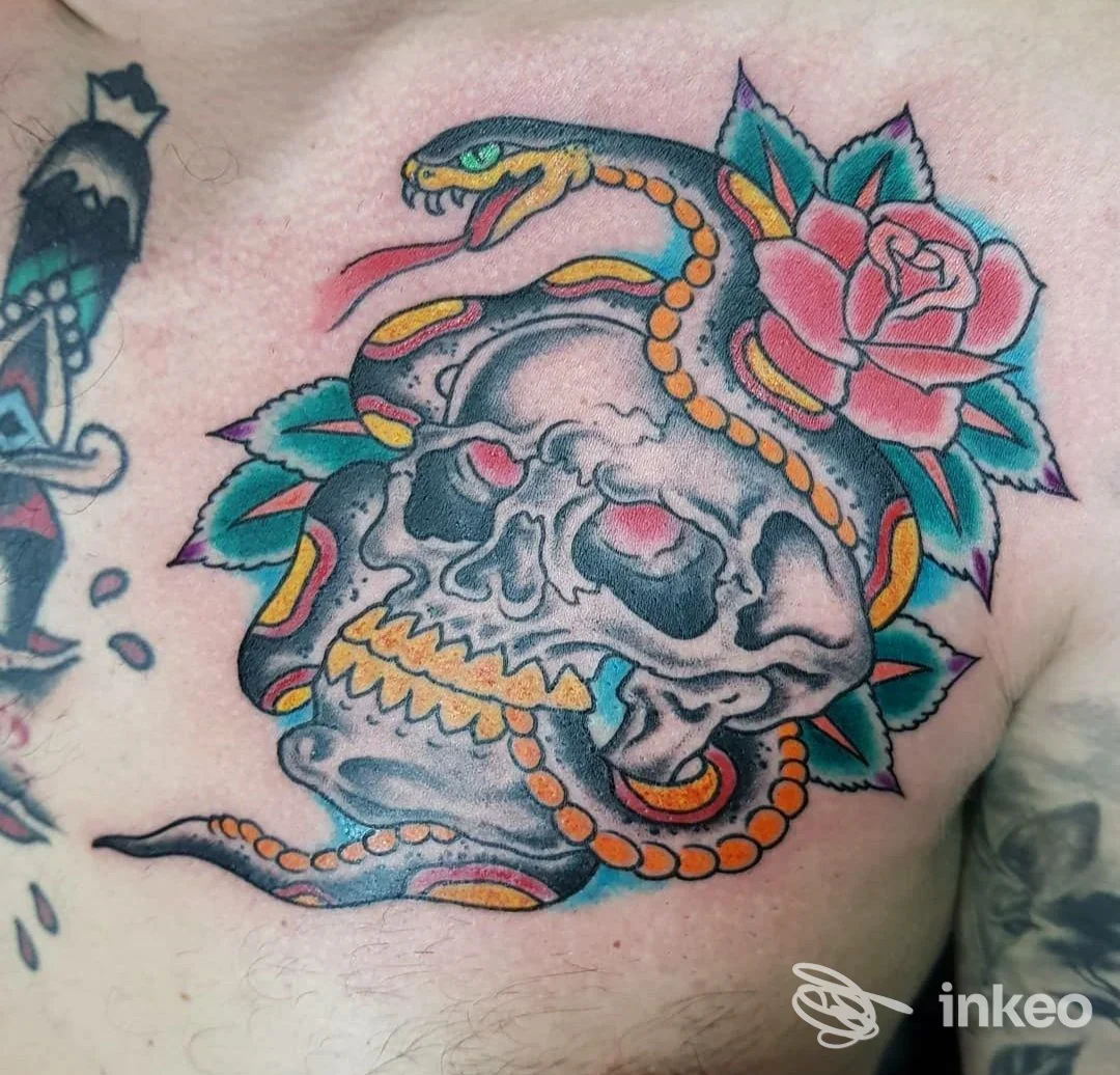 Tattoo colorata sul torace: un teschio grigio con serpente arancione avvolgente e un fiore rosa-rosso vicino, stile tradizionale.