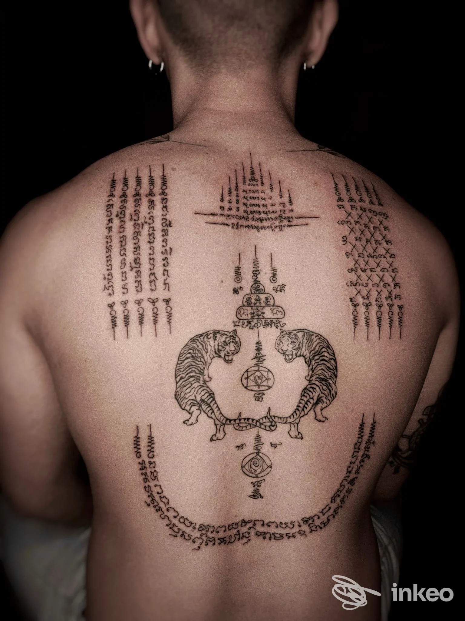 Tattoo reale sulla schiena: due felini ai lati con motivi centrali e simboli, realizzato sulla pelle contro uno sfondo scuro.
