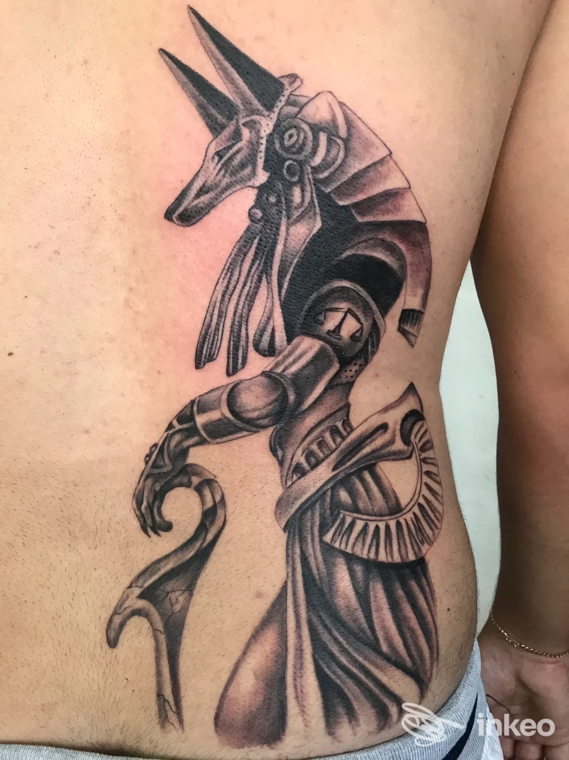 Tattoo in bianco e nero su fianco sinistro, figura stilizzata di animale meccanizzato con dettagli e shading pronunciato, visibile sulla pelle.