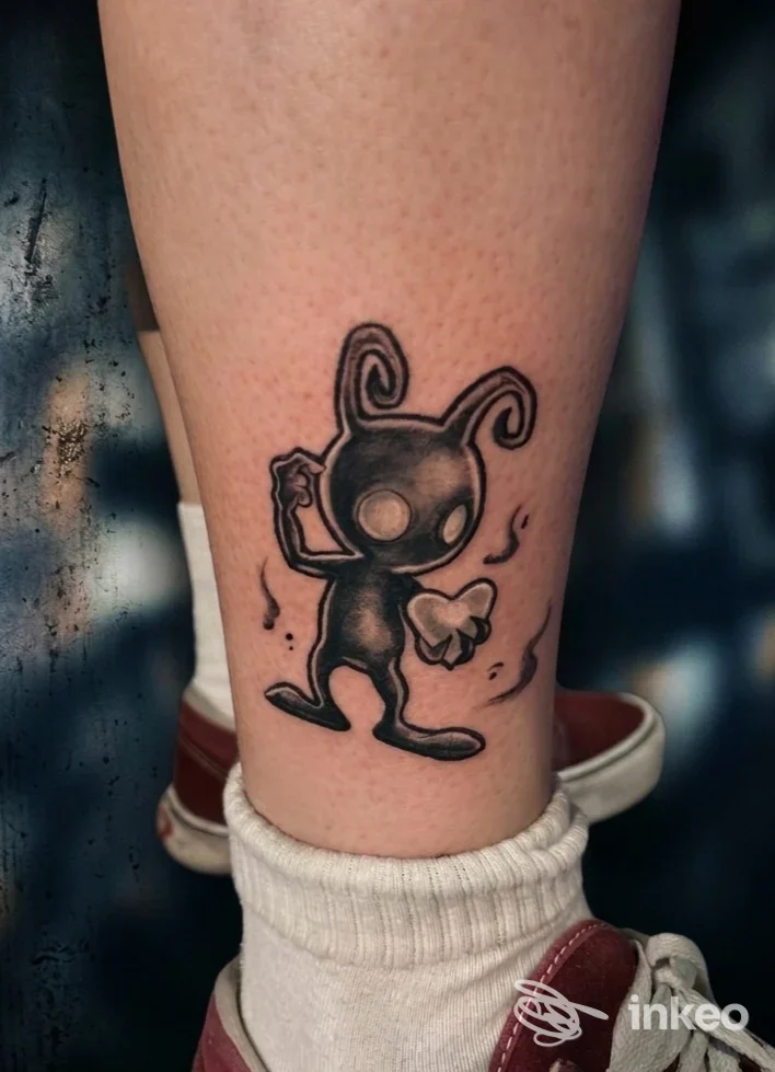 Tatuaggio in stile cartone su polpaccio: creaturina nera con grandi orecchie e zampetta, disegnata in linee scure su pelle chiara.