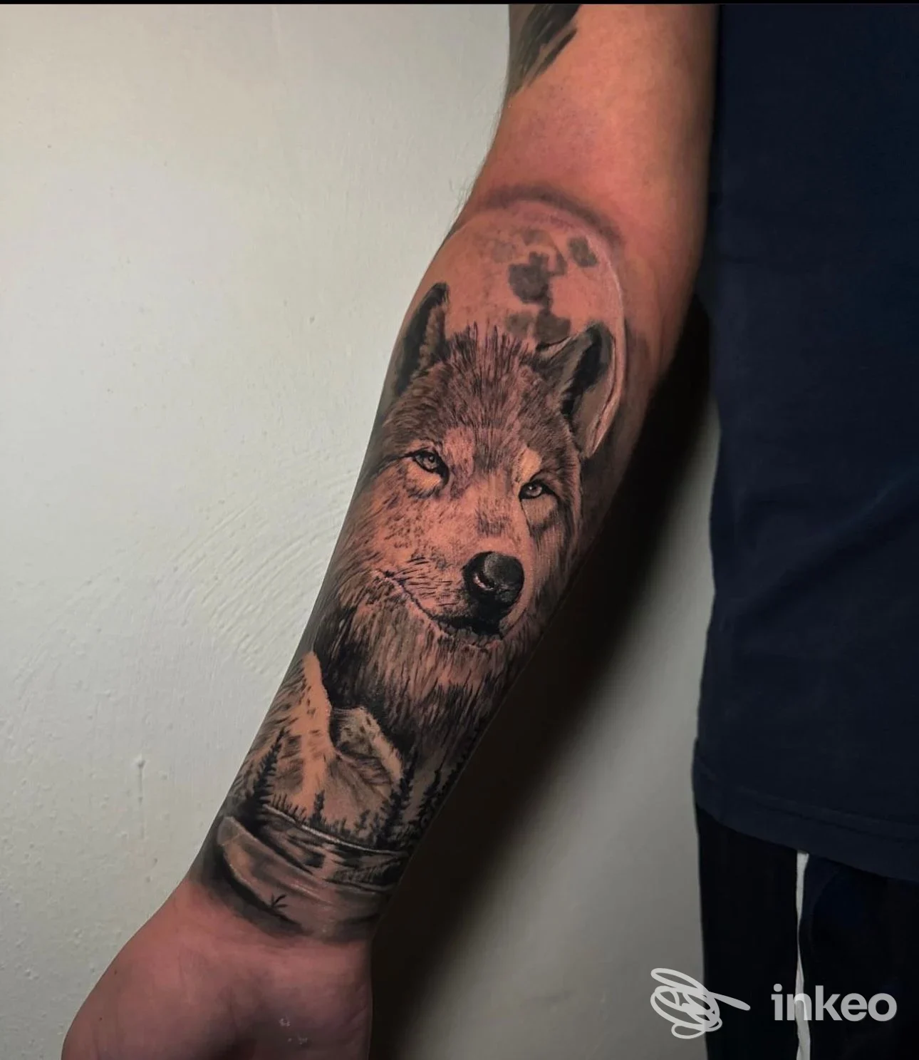 Tattoo realistico di un lupo sull'avambraccio, tonalità in nero e grigio, vista laterale su braccio maschile.