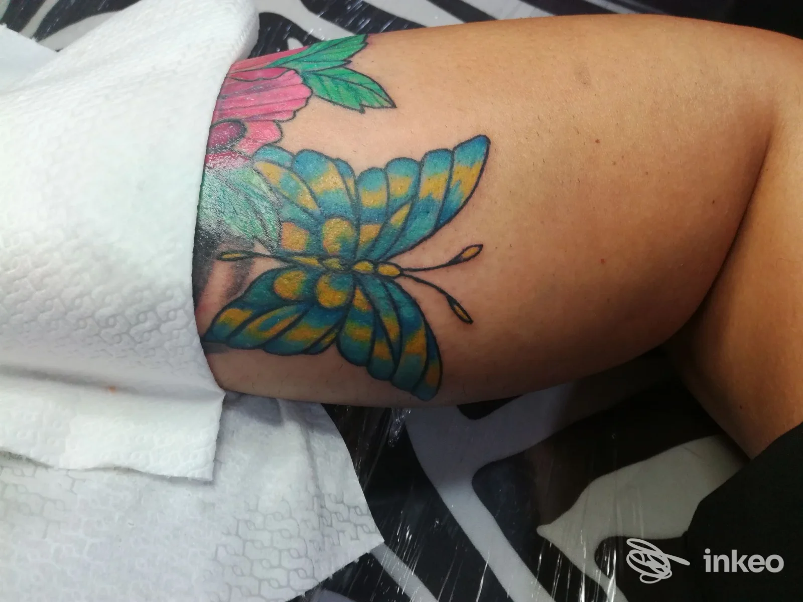 Tattoo colorata a farfalla visibile sulla pelle, parzialmente coperta da un asciugamano bianco, senza viso visibile.