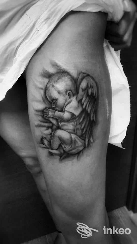 Tattoo raffigurante un bambino angelo alato su braccio, in bianco e nero, realizzato sulla pelle.