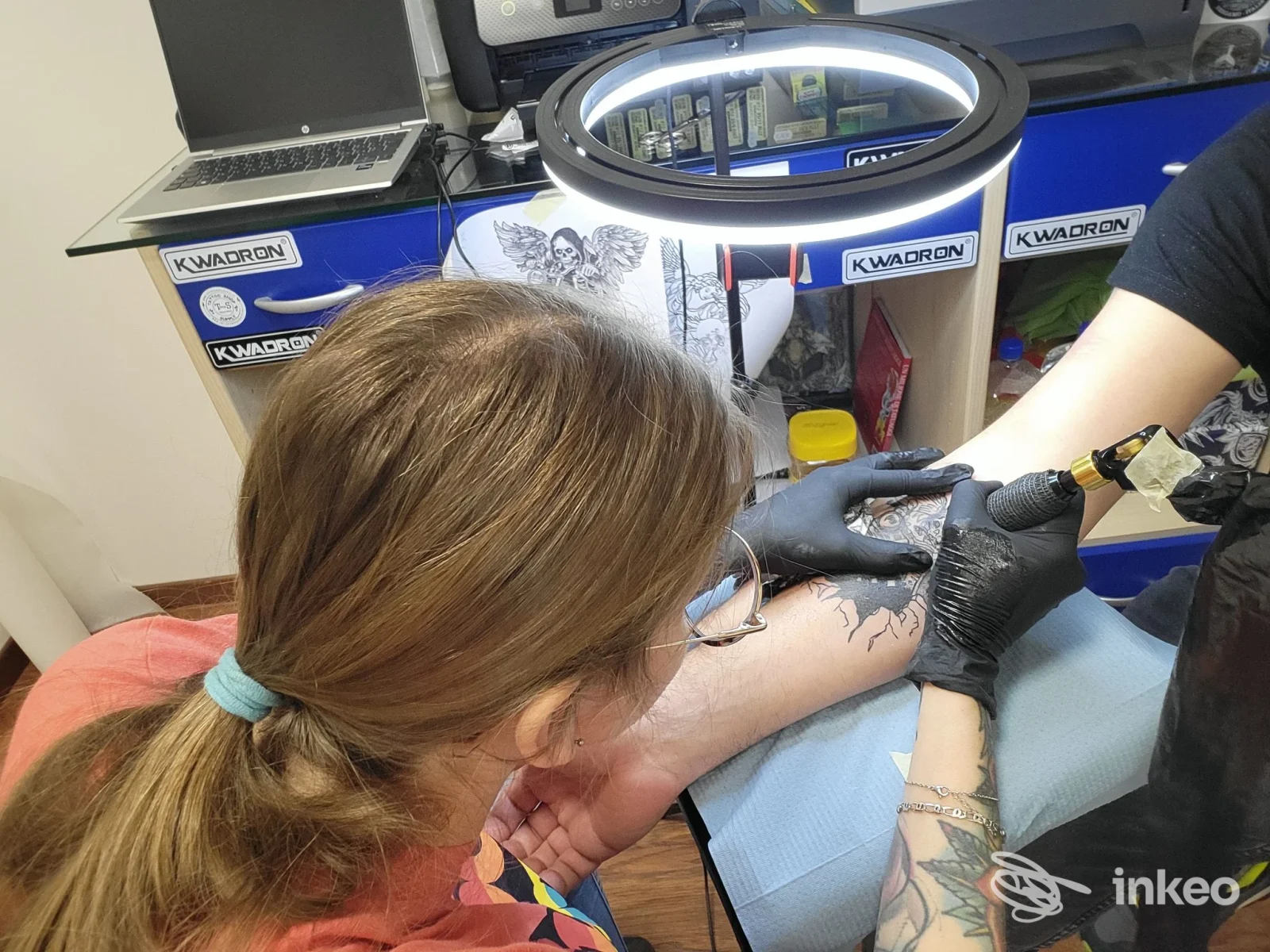 Procedura di tatuaggio in corso su braccio di un cliente nel negozio Lady Hook Tattoo a Villa d'Ogna, con tatuatore al lavoro e lampada circolare.