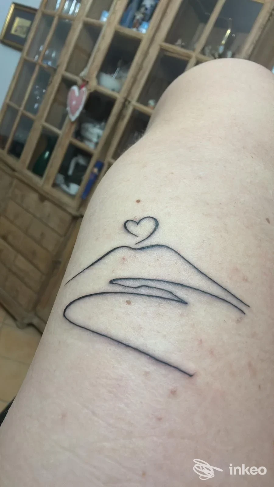 Tatuaggio minimalista a linee nere raffigurante una bocca stilizzata con un piccolo cuore sopra, visibile su parte di avambraccio/piede della persona.