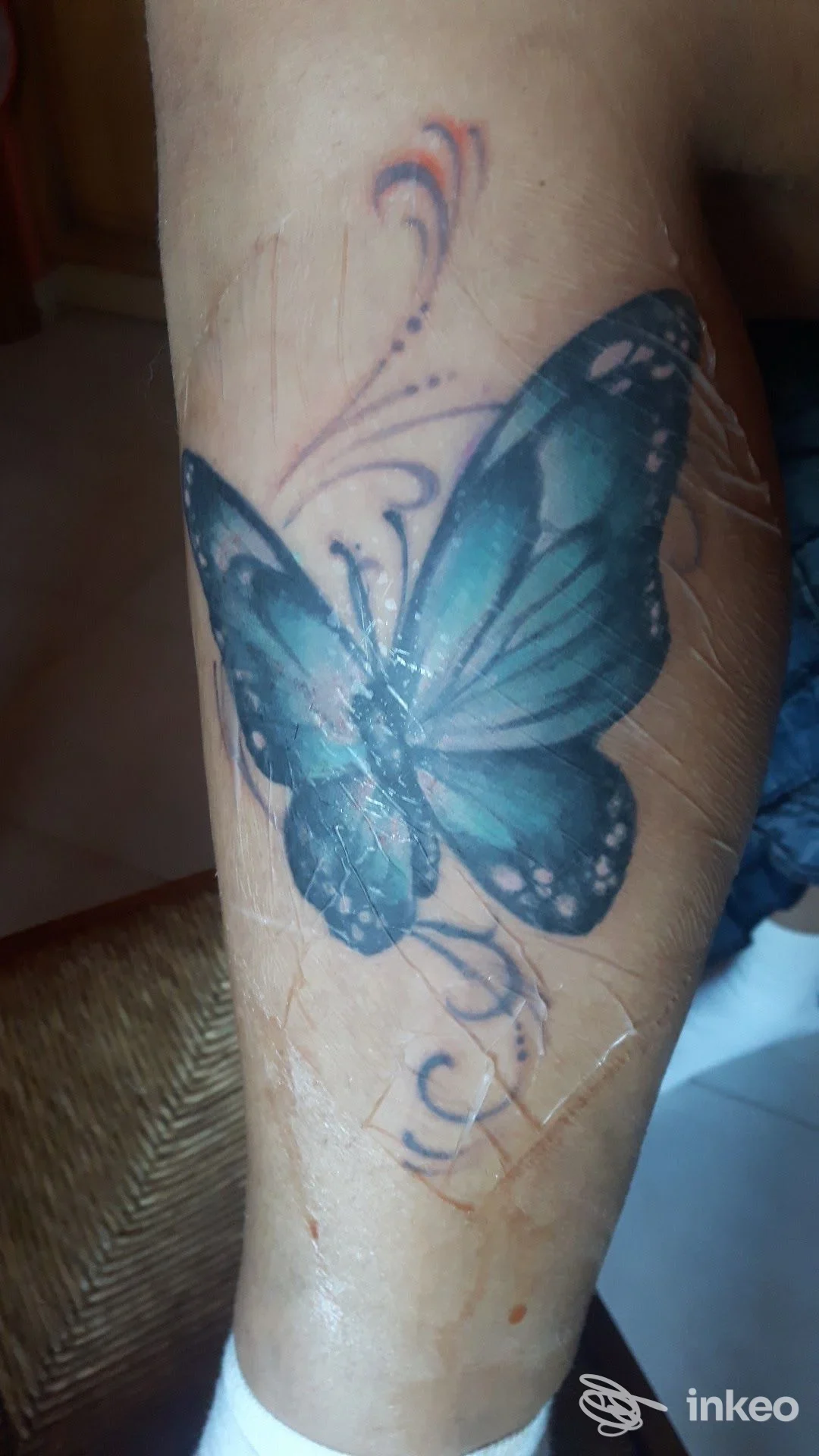 Tattoo reale di farfalla blu sulla gamba, scatto dall'angolazione laterale; nessun overlay o testo promozionale visibile.