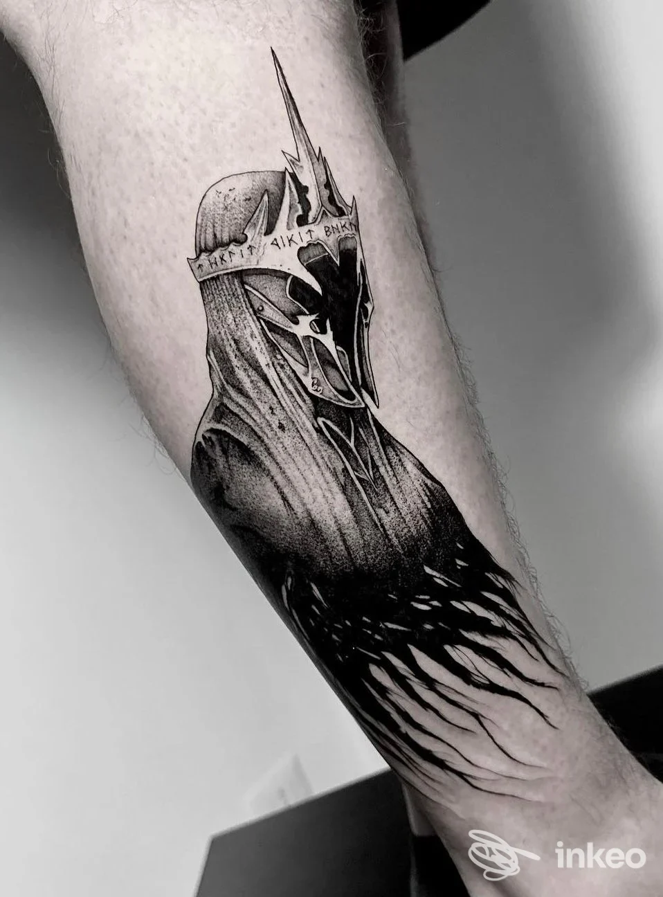 Tatuaggio in bianco e nero su avambraccio raffigurante una figura stilizzata con elmo o maschera, sfumature leggere lungo il braccio.