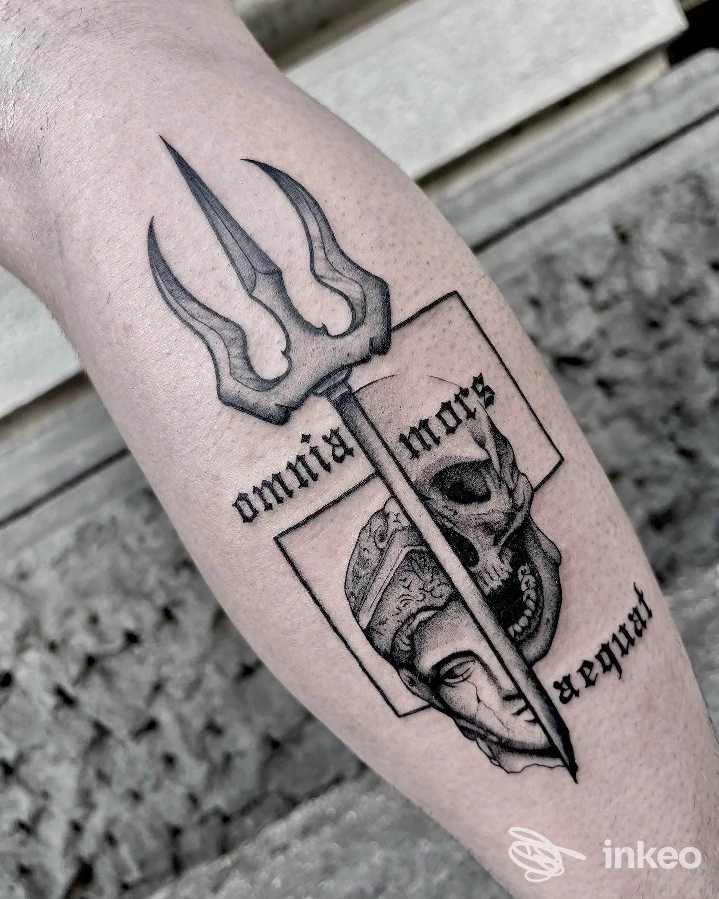 Tattoo visibile su avambraccio: disegno in nero con tridente e figura mascherata all’interno di una cornice; braccio e pelle visibili, nessun volto completo, testo o interfacce social.