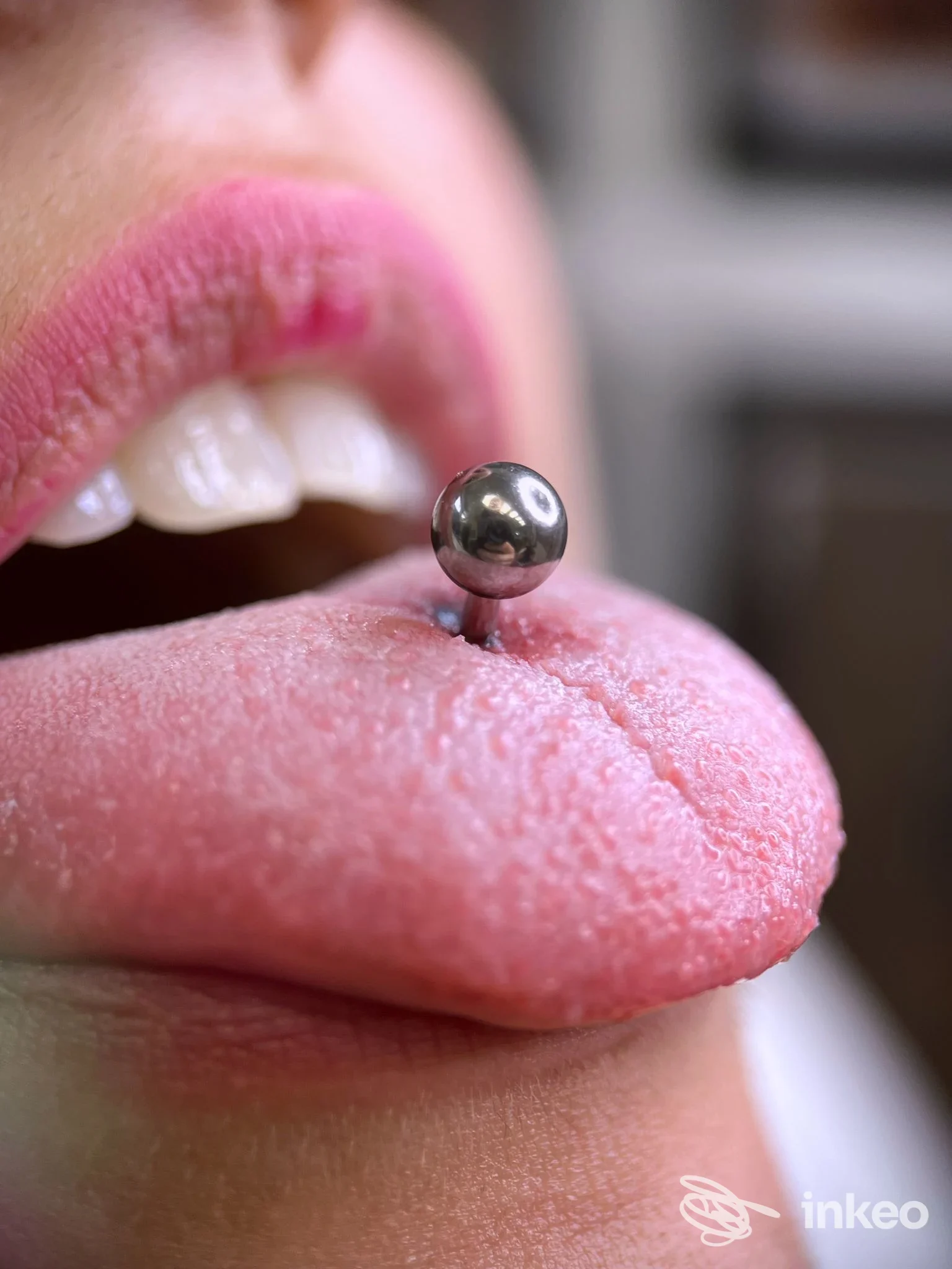 Piercing alla lingua con pallina metallica, visibile su labbra e lingua di una persona, scatto ravvicinato.