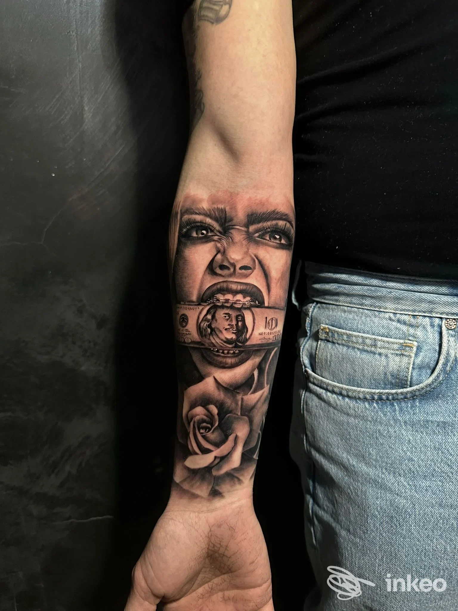 Avambraccio sinistro di una persona con un tatuaggio realistico che mostra una faccia, una banconota e una rosa; studio Marble Tattoo Studio a Battipaglia.