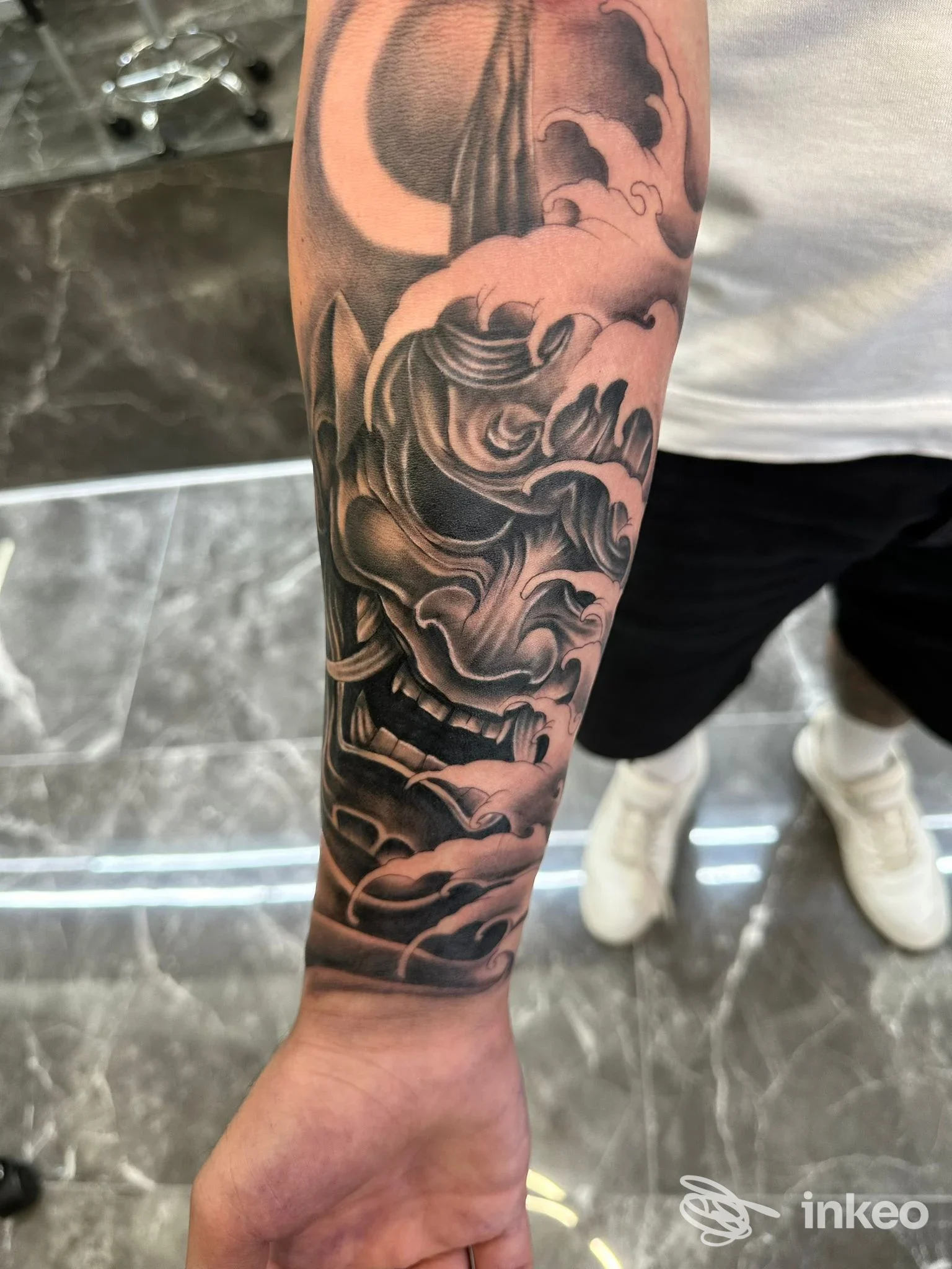 Tatuaggio in bianco e nero sull'avambraccio, con sfumature e dettagli scultorei, senza visibilità del volto.