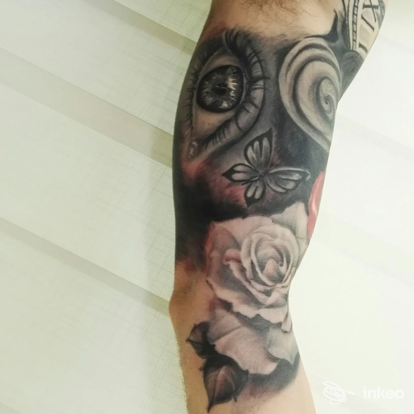 Braccio visibile con tatuaggio realistico: rose, insetti e motivi floreali in tonalità grigie e neri, dettagli di luce e sfumature, alta definizione.