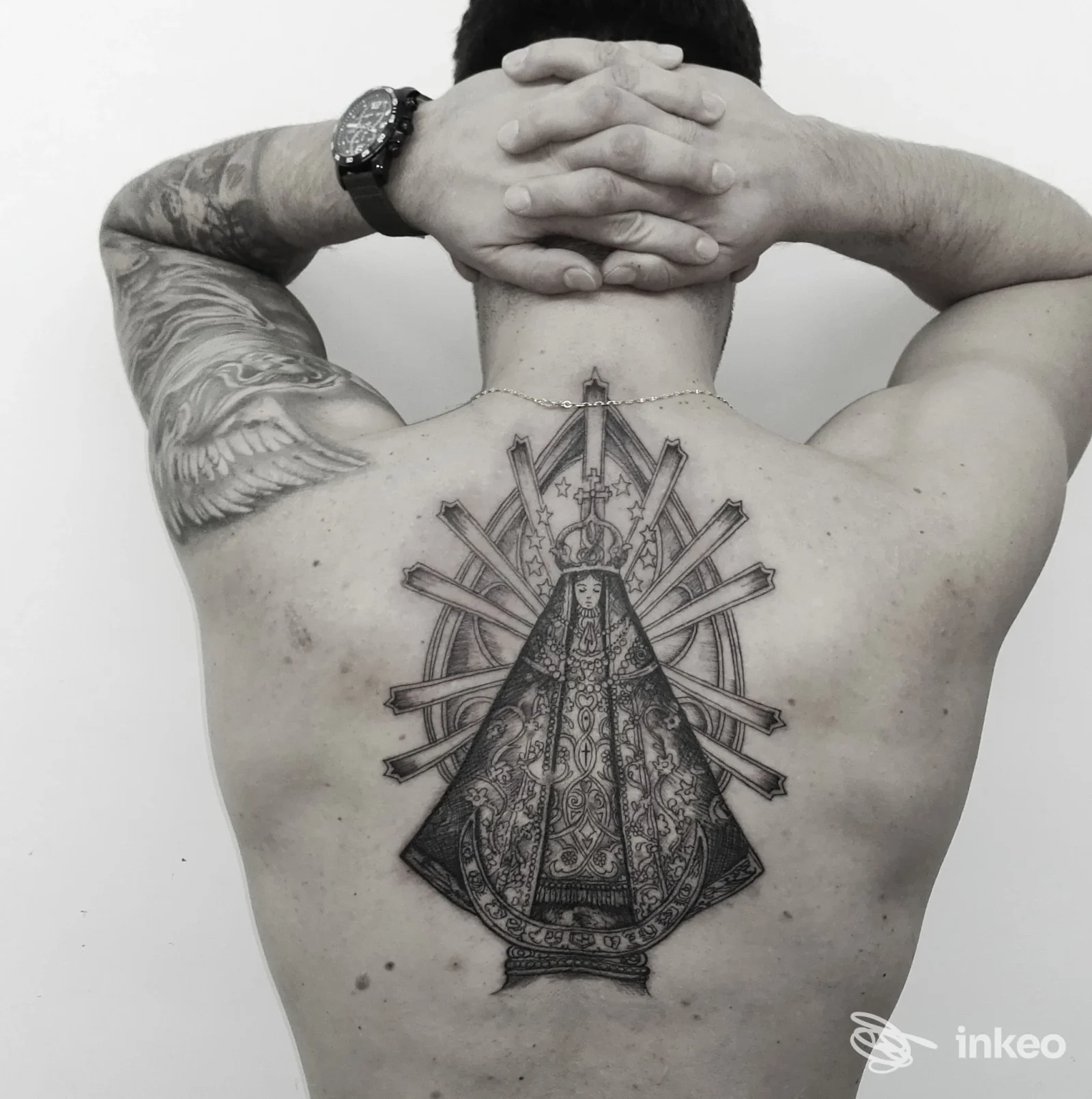Tattoo religioso sul dorso di un uomo, grande motivo centrale con figura sacra, braccia piegate e mani dietro la nuca.