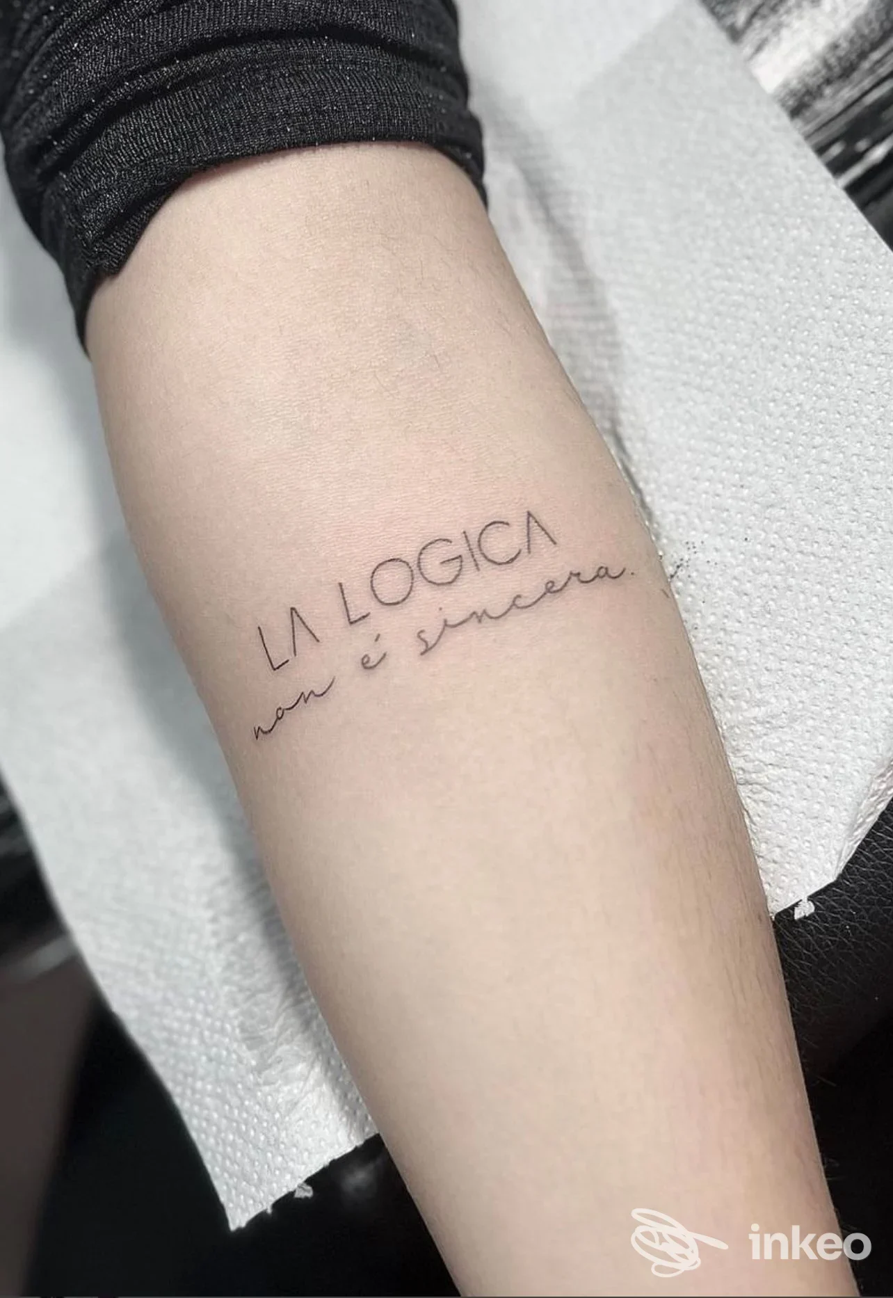 Avambraccio visibile con tatuaggio testuale sottile: 'LA LOGICA' seguito da parole leggibili, senza volto visibile, scatto con illuminazione neutra; The Red Queen Tattoo, Cava de' Tirreni.