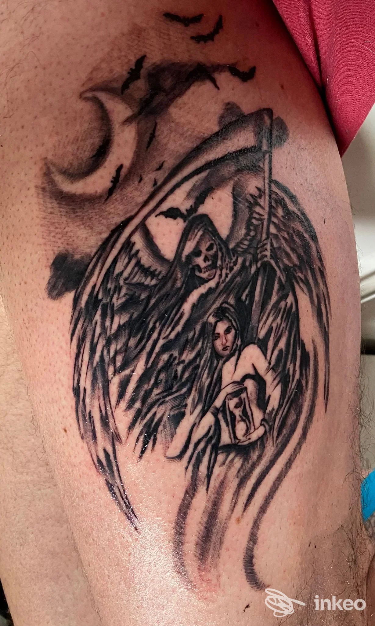 Tattoo su braccio raffigurante un angelo con ali nere e una figura femminile al centro, con sfumature in bianco e nero, stile graphico realistico.