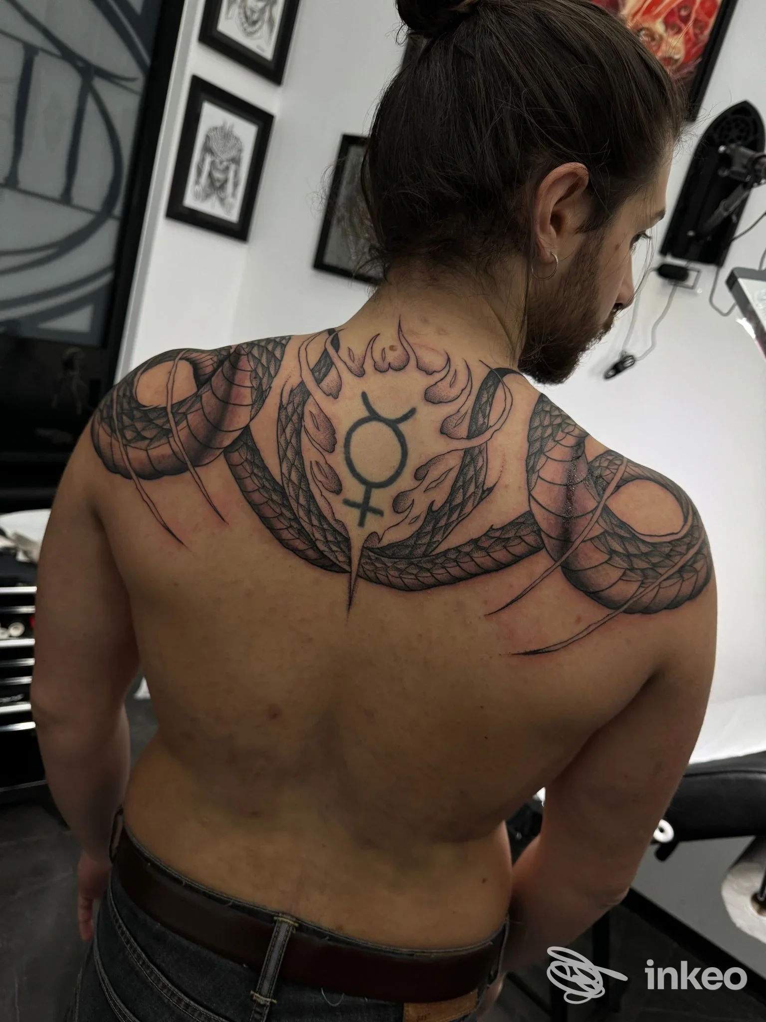 Schiena di un uomo con tatuaggio grafico e serpenti attorno alla spina dorsale, visibile dall'angolazione posteriore in studio, firma un disegno permanente sulla pelle.