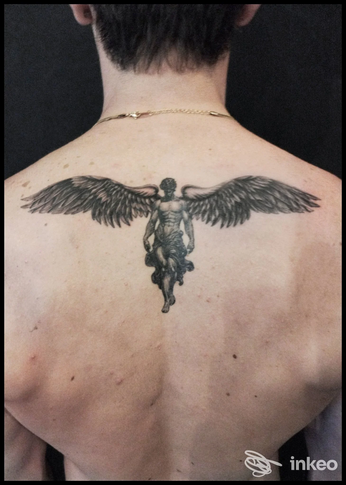 Tattoo sulla schiena di una persona: ali d'angelo con figura al centro, vista da dietro, tono scuro e dettaglio nitido.